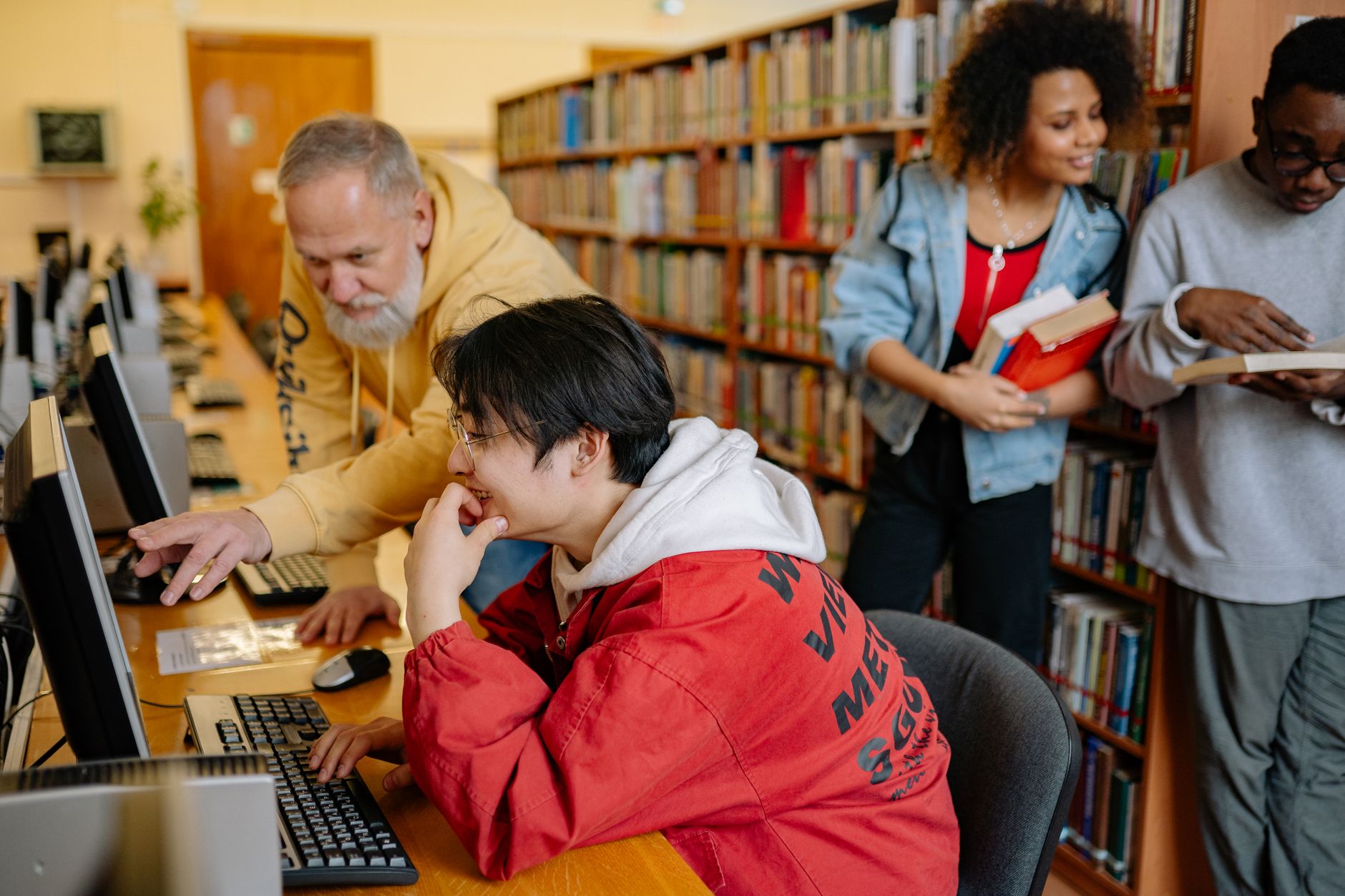 Network SecurityC#.NET Programming — Students collaborating and learning in a library setting, engaging with computers and books.