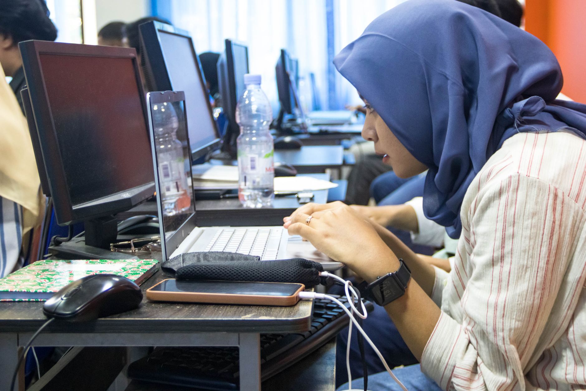 Elective Units — A young woman in hijab using a laptop in a computer classroom setting.