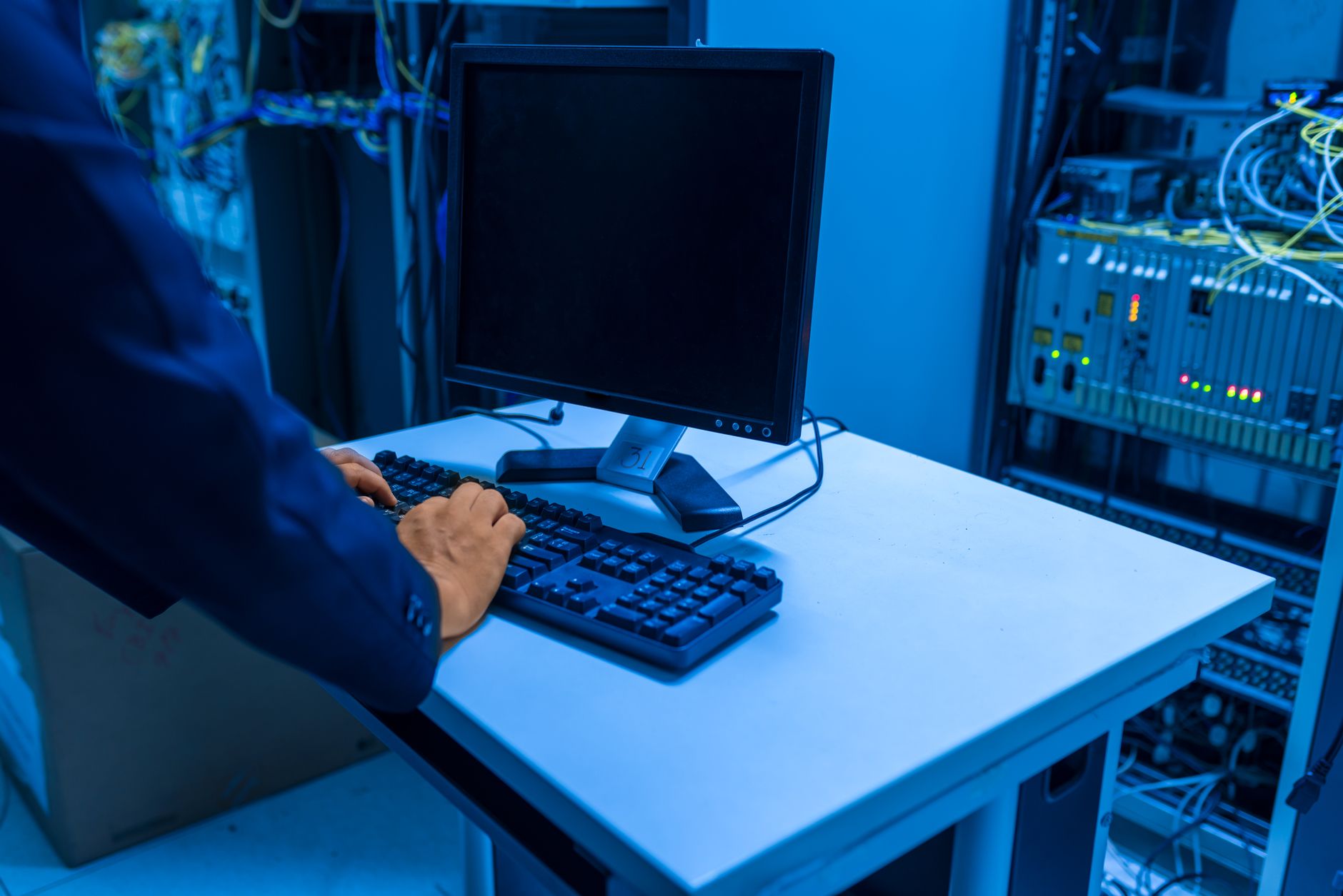 System Administration — An it professional operates a computer in a server room, managing network systems and connected devices.