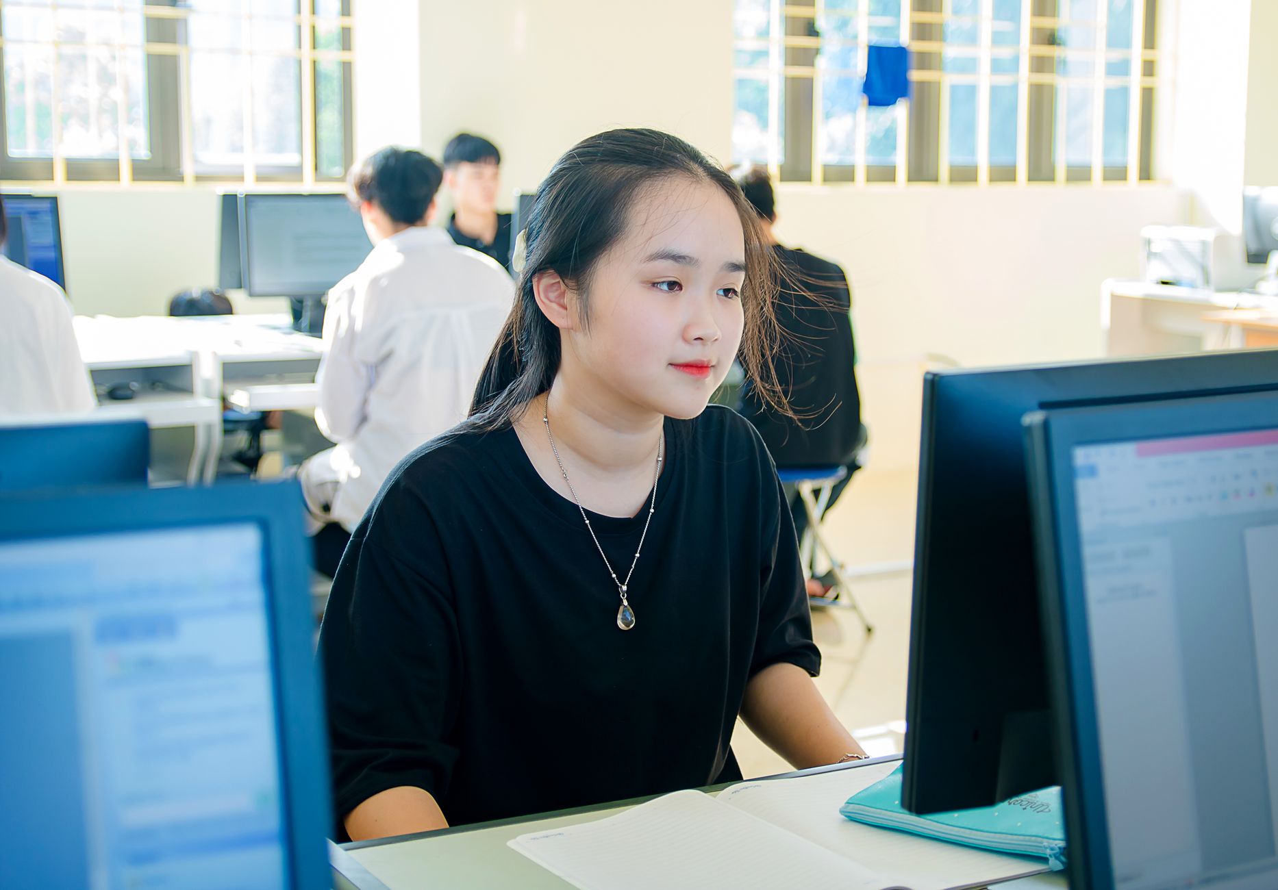 Network SecurityC#.NET Programming — A young asian woman concentrating on a computer screen in a university classroom.