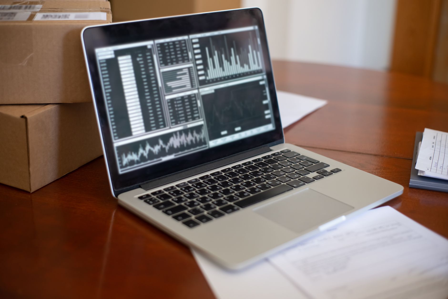 Business to Business (B2B) E-commerce — Laptop showing data graphs on wooden table with cardboard boxes, depicting a small business office setting.