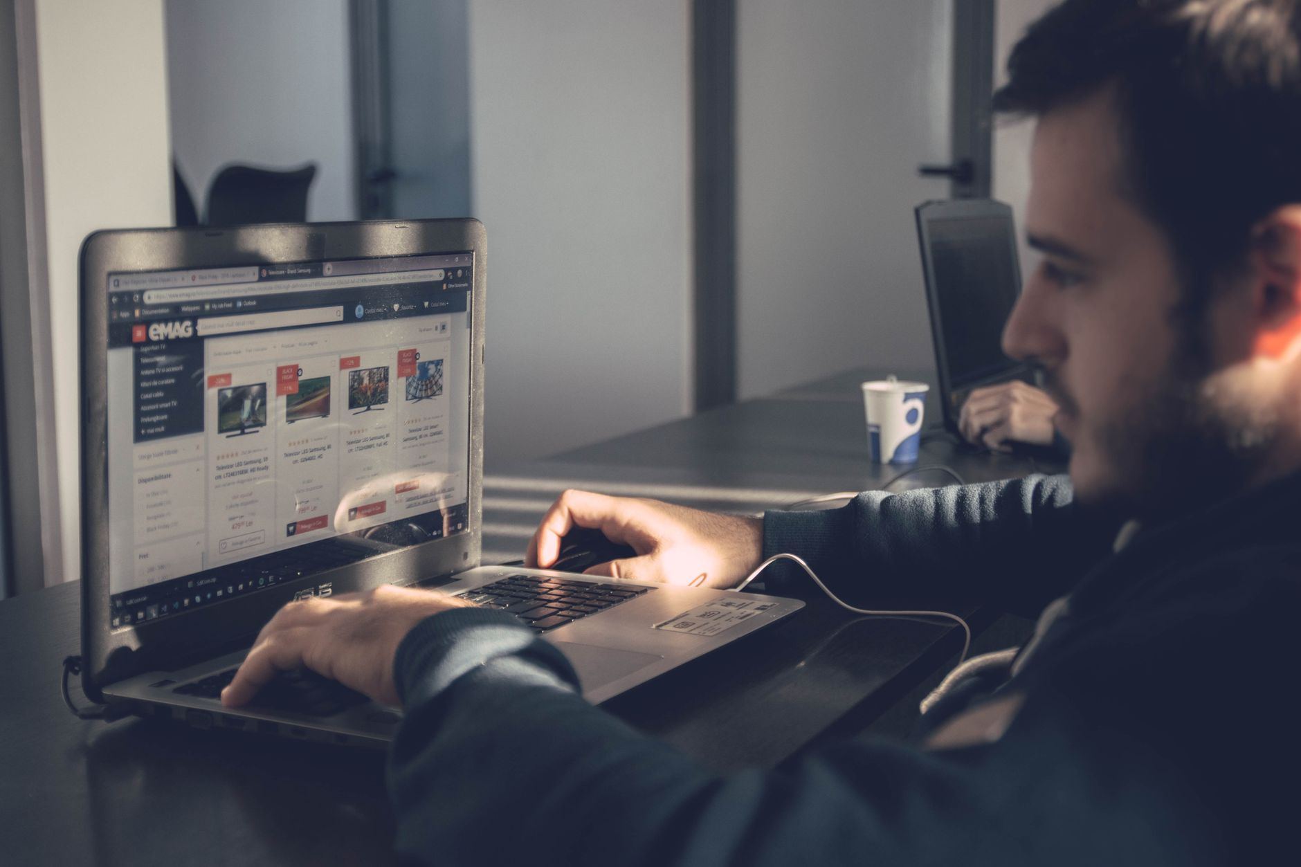 Business to Business (B2B) E-commerce — Adult man using laptop to browse an online marketplace in a modern office.