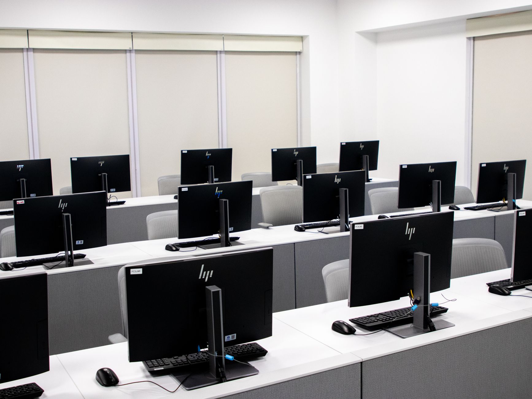 Physical IT Networking — Spacious and minimalist computer lab with rows of black monitors and sleek furniture.
