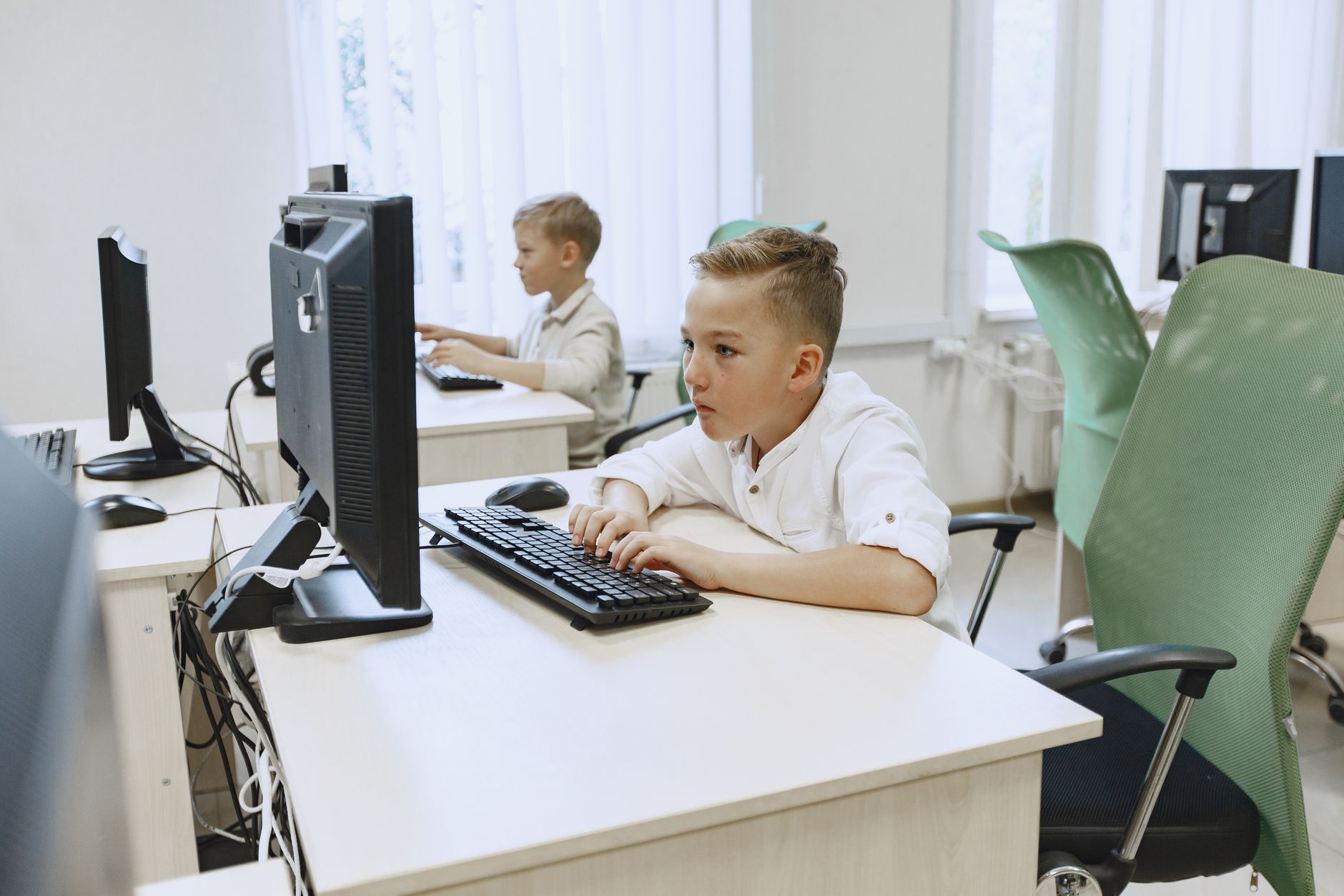 Technopreneurship — Two young boys focused on computers in a bright, modern classroom setting.