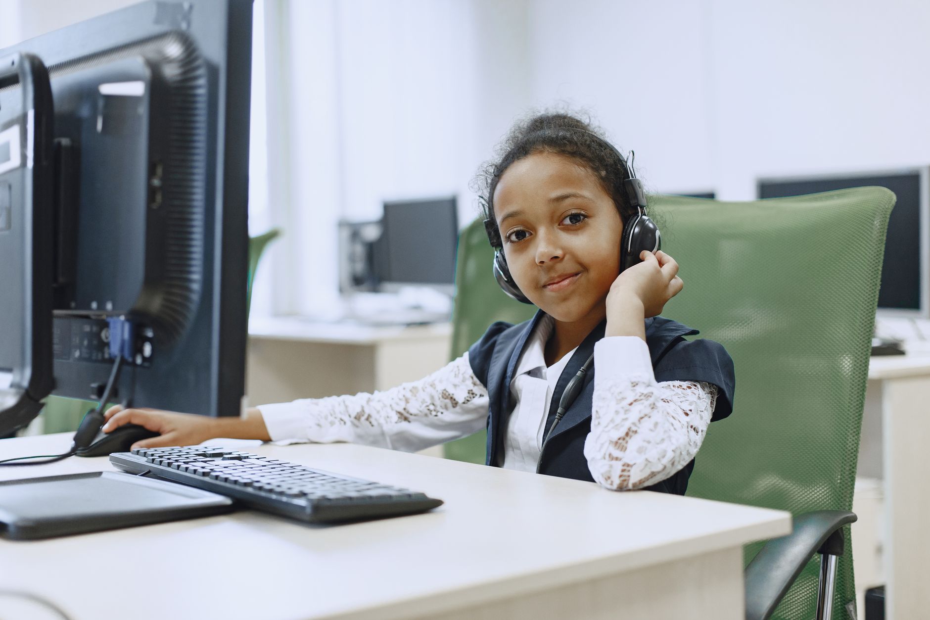 All 12 units are — An african american girl with headphones using a computer in a modern classroom setting.