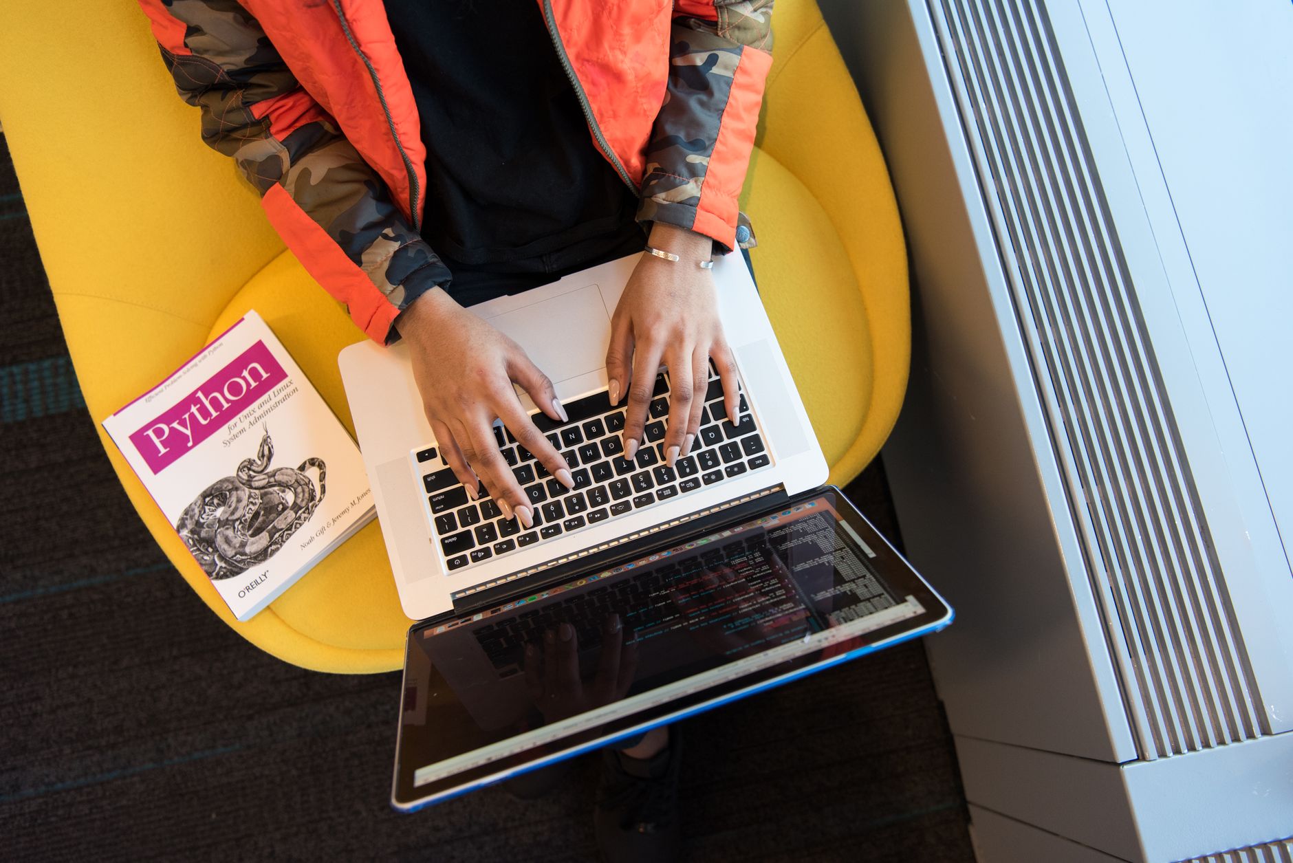 Python for Data Science — High-angle view of woman coding on a laptop, with a python book nearby. ideal for programming and tech content.
