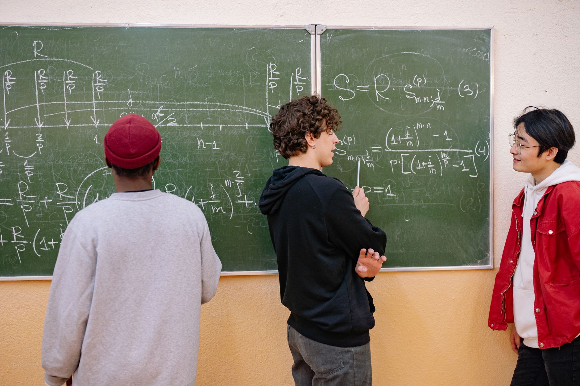 Mathematical Foundations for Machine Learning — Three students discuss math equations on a classroom blackboard, fostering learning and teamwork.