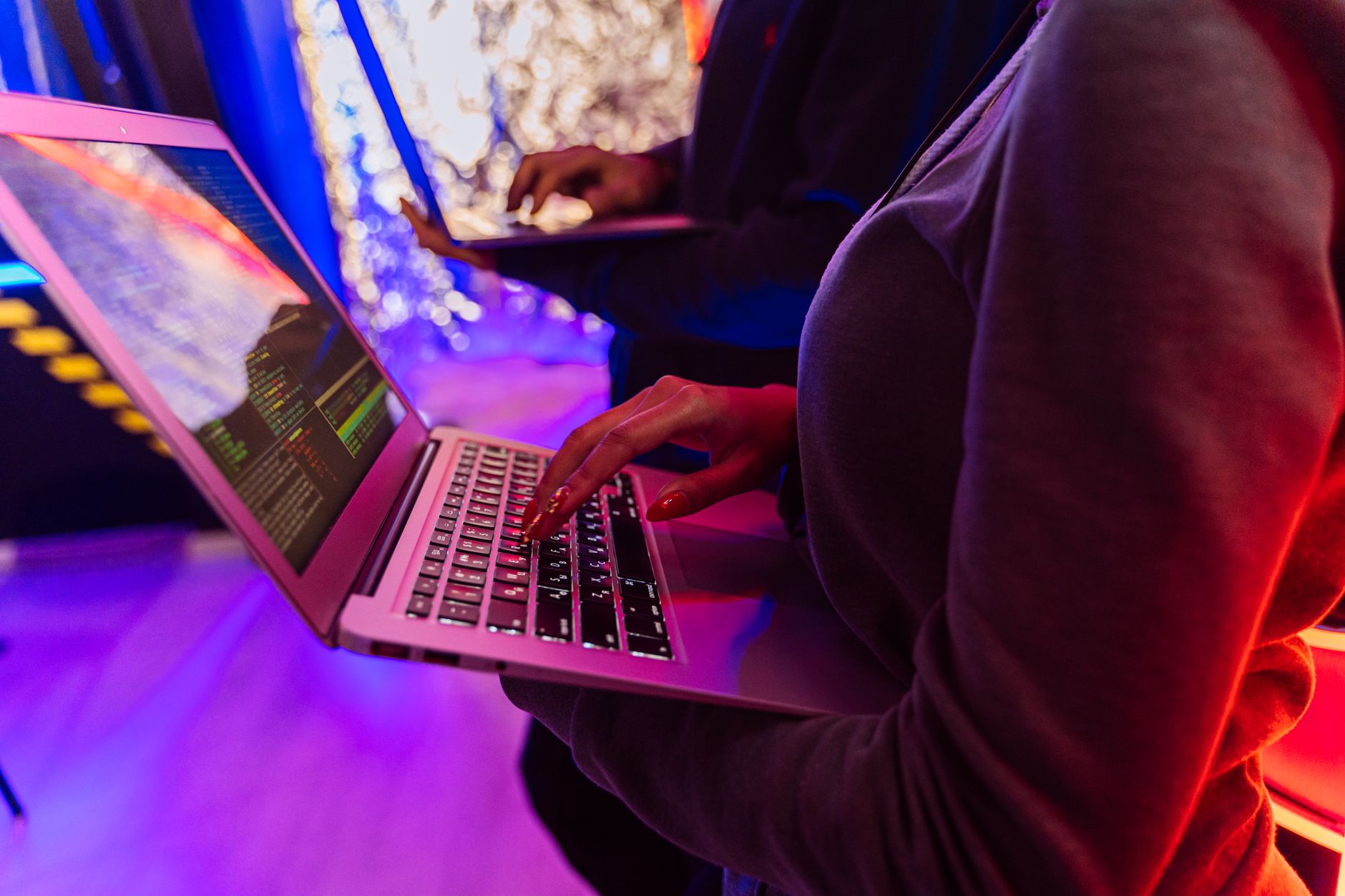 Threat and Risk: Expecting the Unexpected — Two professionals analyzing data on laptops with colorful lighting, focusing on cybersecurity details.