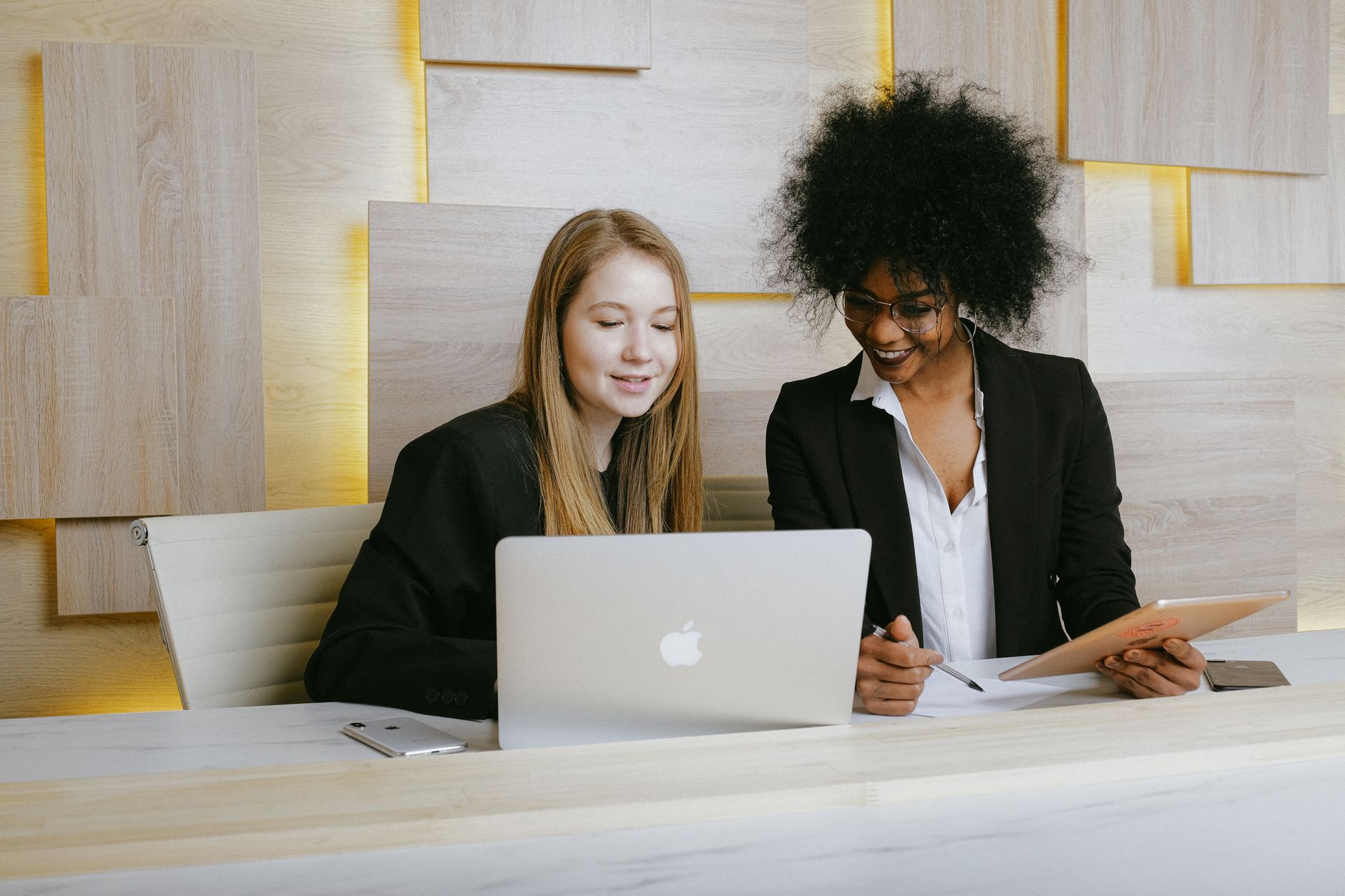 Human Resource Management — Two businesswomen collaborating in a modern office setting, discussing work over a laptop.