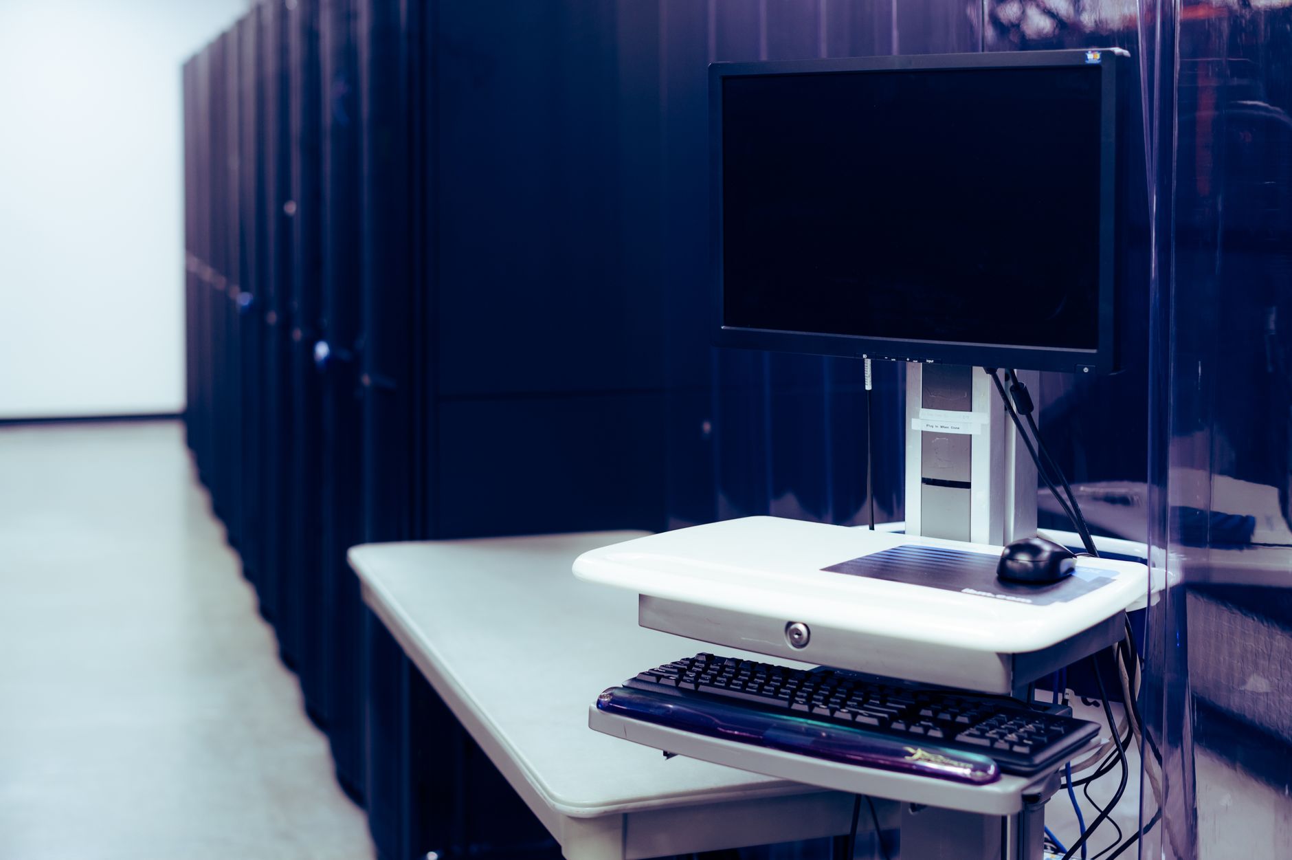 Computer Systems — Contemporary computer with black screen placed on stand near row of server steel racks in data center
