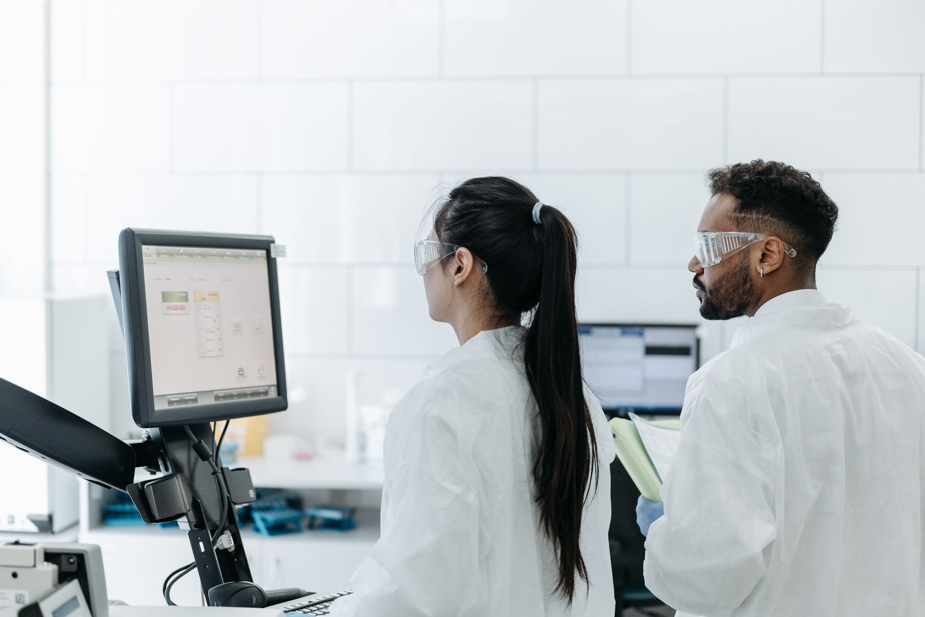 Investigations and Incident Response — Two scientists wearing lab coats and goggles analyze data on a computer in a modern laboratory.