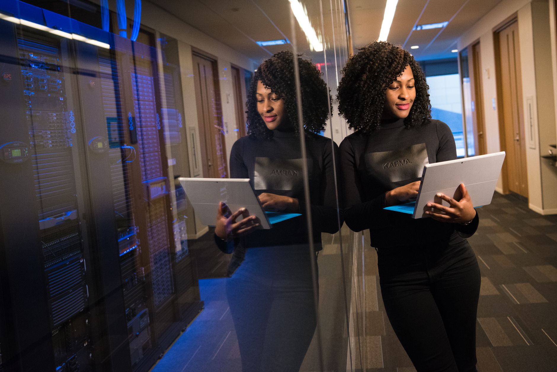 Network Security and Data Communications — African american woman standing in modern office using laptop, reflecting professionalism and technology engagement.