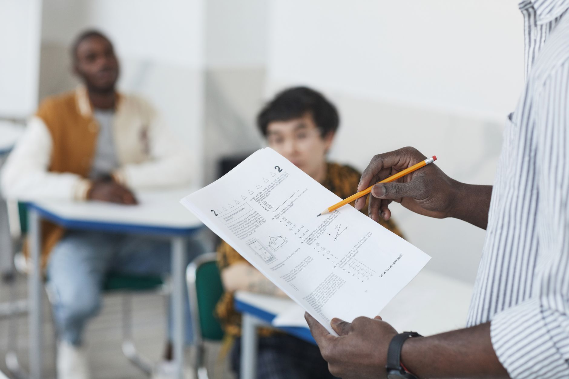 Legal requirements in childcare — Students working on an exam with a teacher overseeing in a classroom.