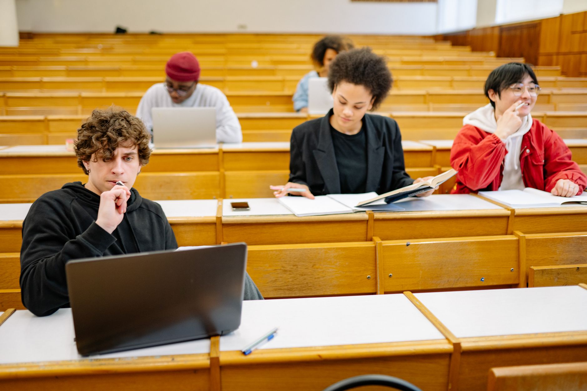 Caring for children through play out of school — A diverse group of college students studying in a classroom setting with laptops and books.
