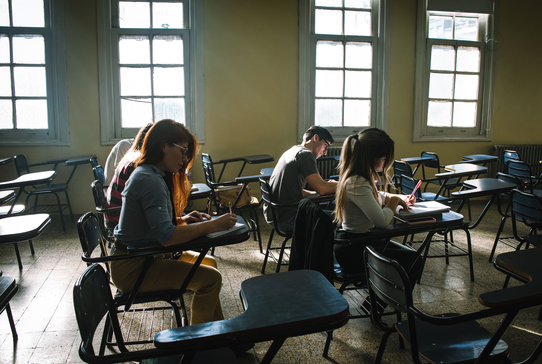 Child development and communication skills in early years — Students focused on writing during an exam in a sunlit classroom.