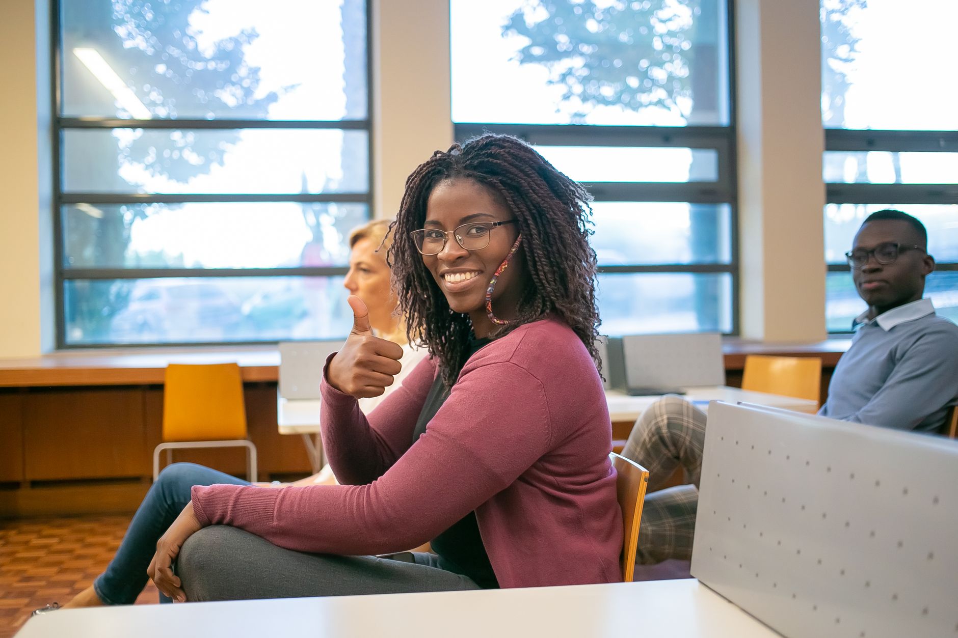 Developing children’s mathematical skills — Side view of positive african american female student demonstrating like sign while sitting at lecture with classmate and teacher