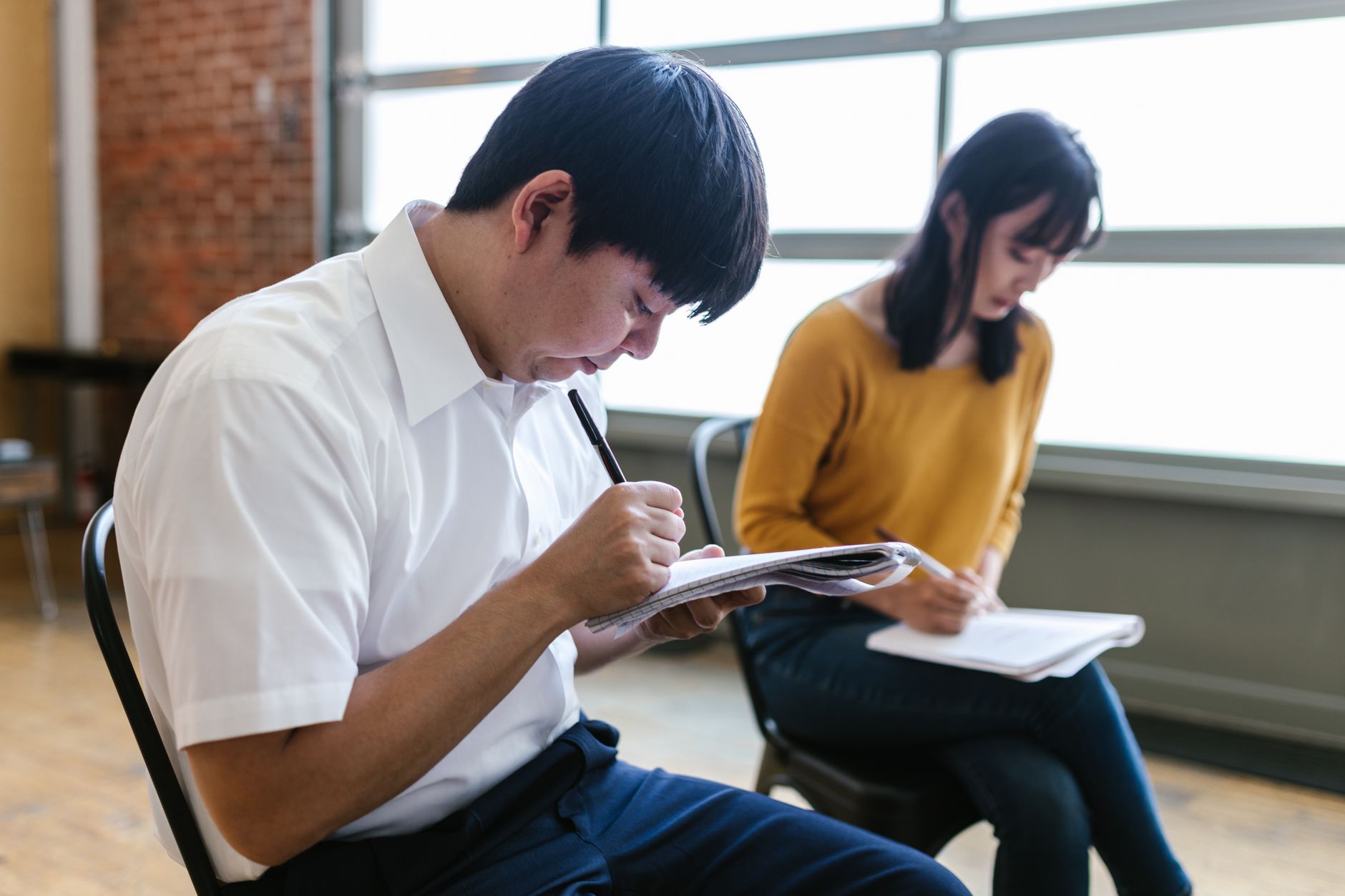 Safeguarding in early years — Two students intensely taking notes during a lecture inside a modern classroom.