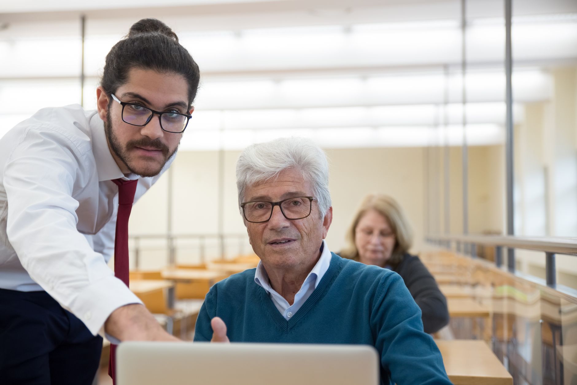 Design of Education and Training Resources — An elderly man learning computer skills with a teacher in a classroom setting, showcasing education through technology.