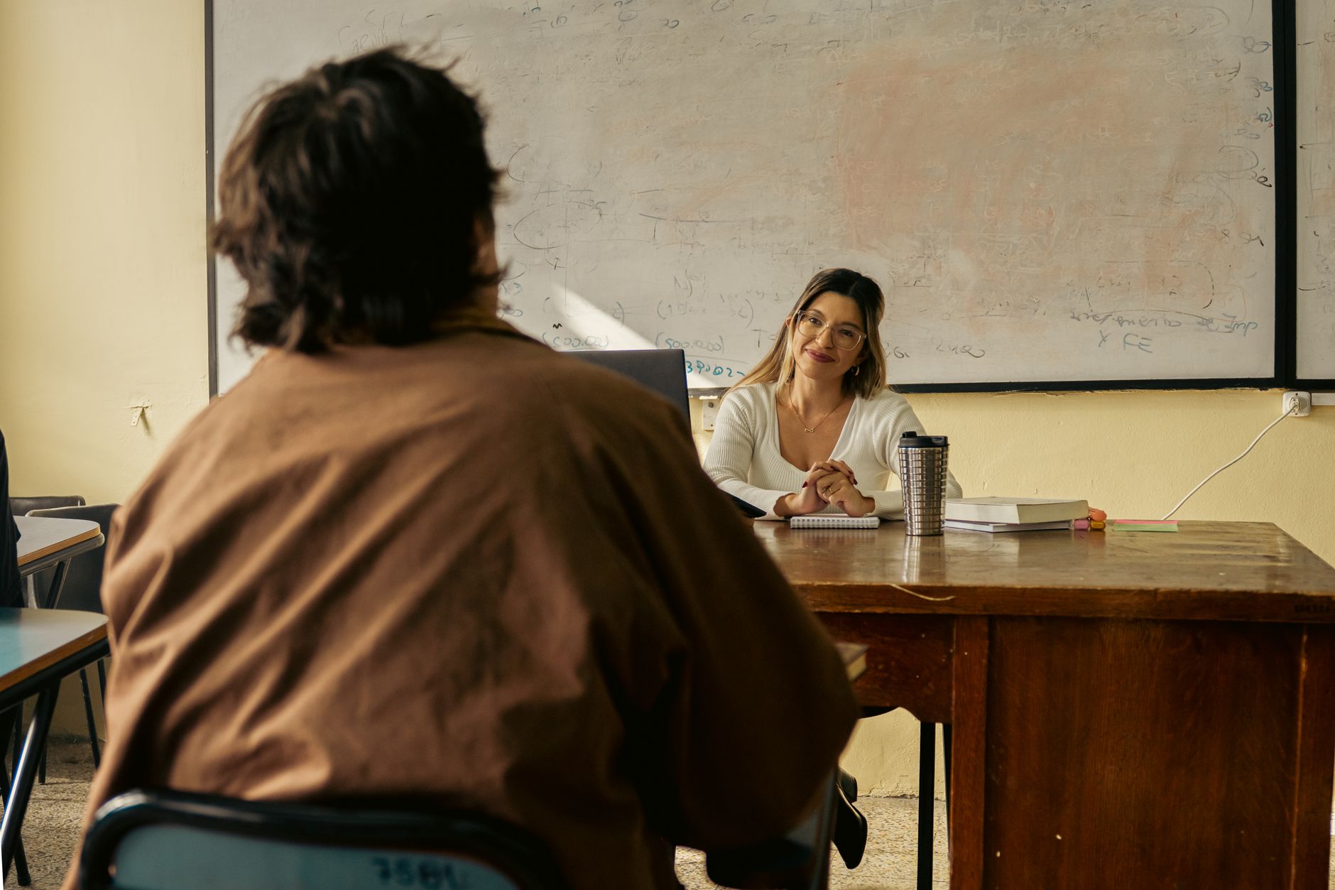 Develop and Prepare Resources for Learning and Development — A teacher engages with a student in a university classroom setting, fostering learning.