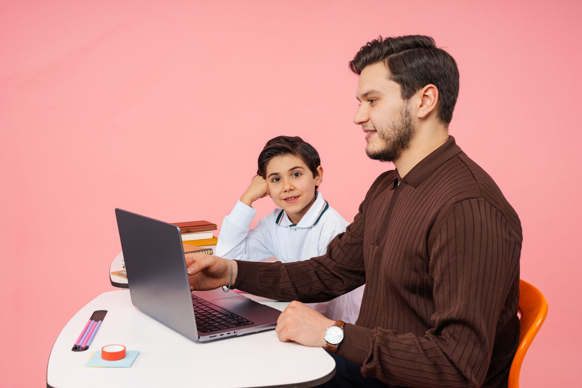 Leadership Qualities and Practice in Education — A teacher helps a student with laptop learning against a pink background in yalova, türkiye.