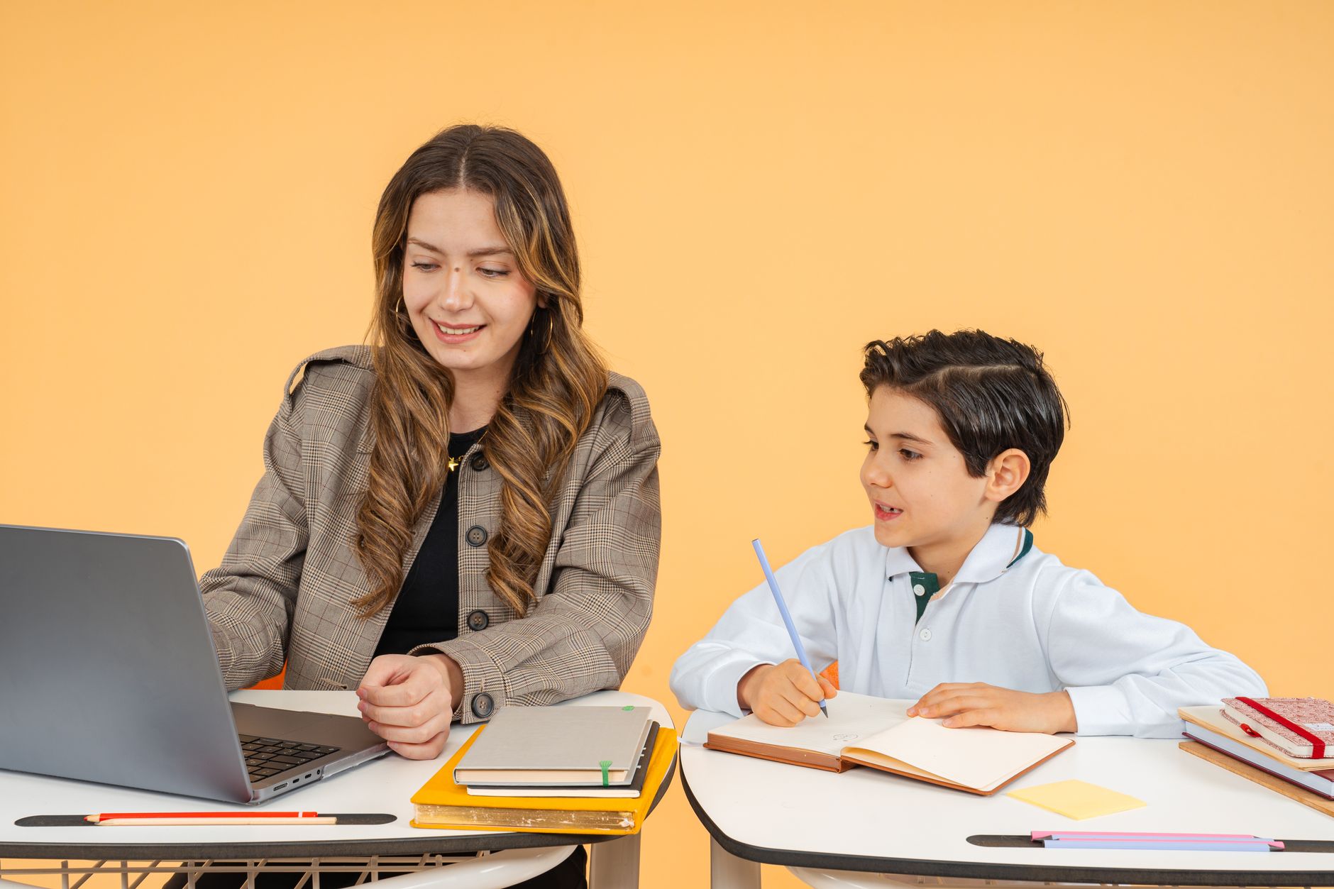 Teaching Productive Skills: Speaking and Writing — A female teacher helps a young student with his studies using a laptop in a classroom setting.