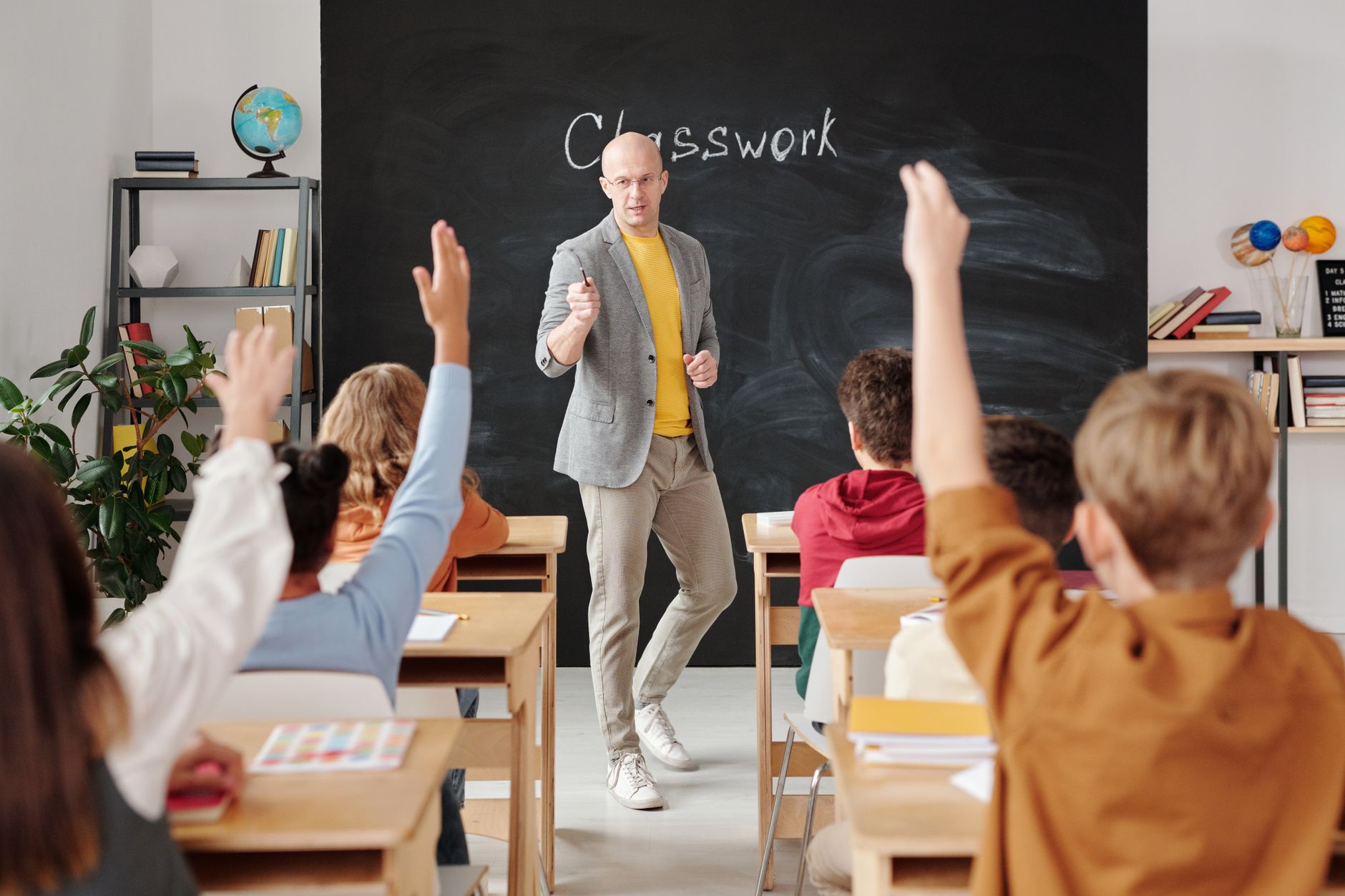 Principles of Teaching and Learning Theory and Practice — Teacher interacting with students raising hands in a classroom setting.