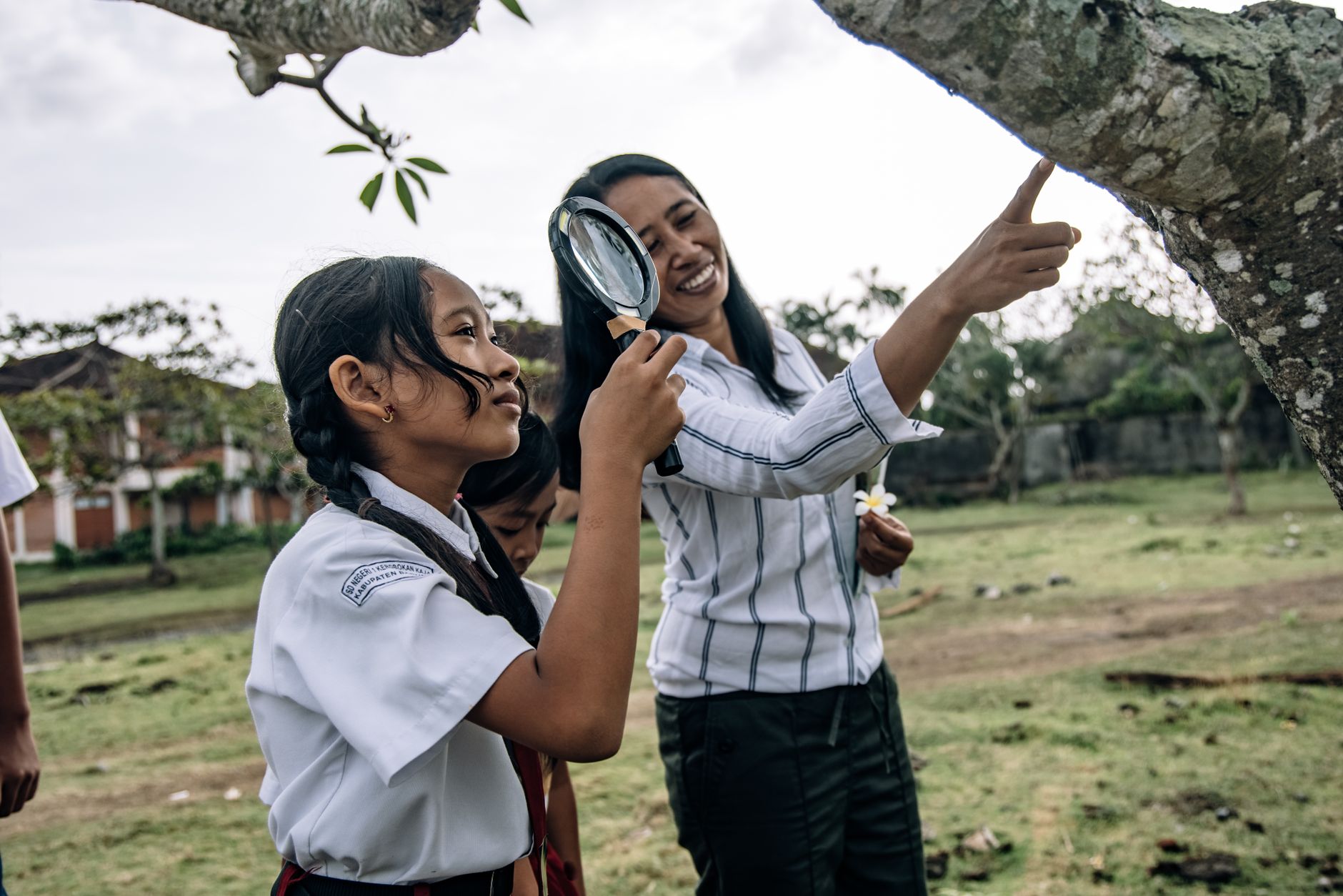 Developing Evidence-Based Global Teaching Practice — Students in school uniforms explore nature with a teacher using a magnifying glass.