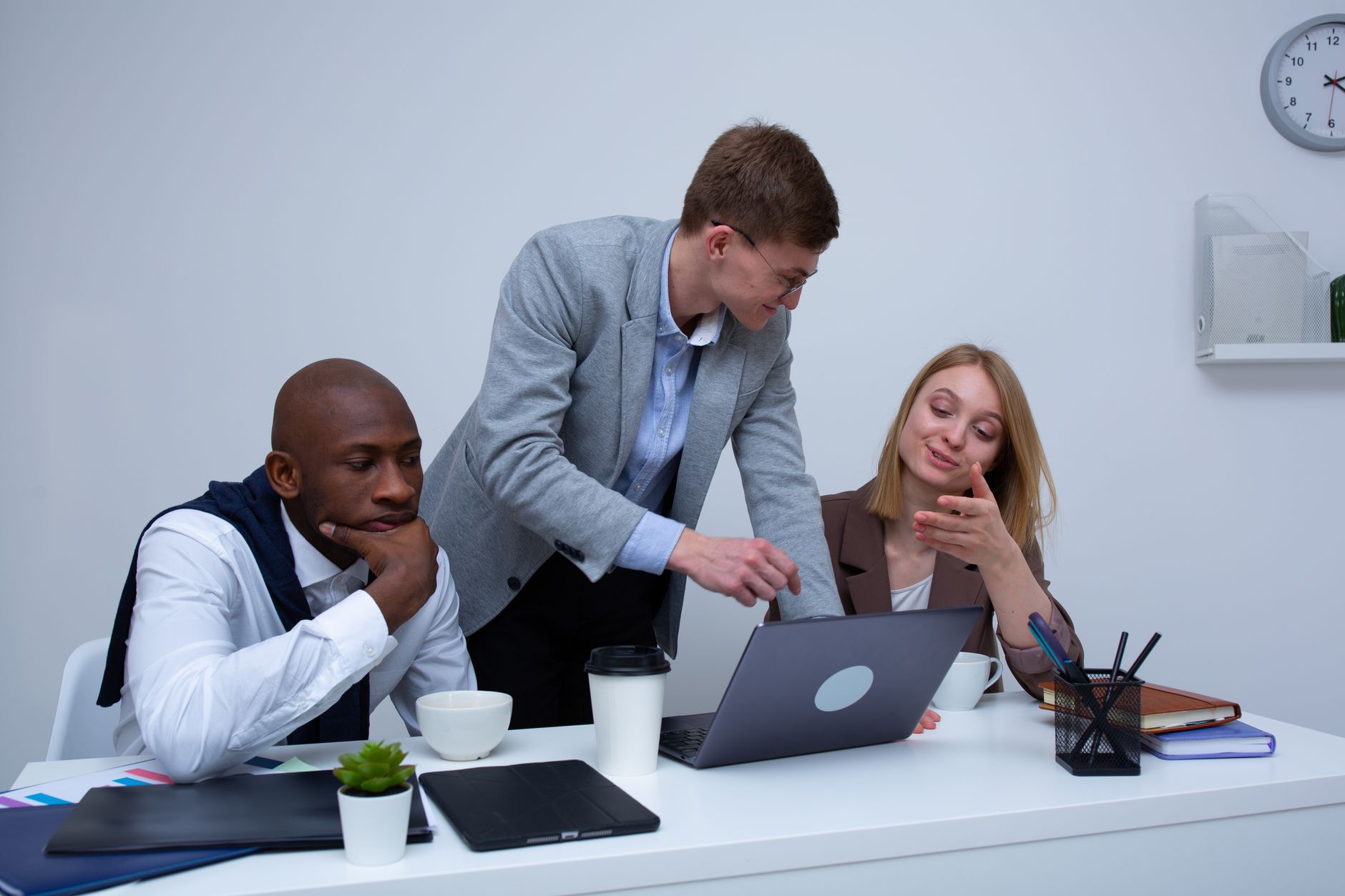 Manage Progress and Accountability in a Coaching Environment — A diverse team collaborating in a modern office environment, discussing work on a laptop.