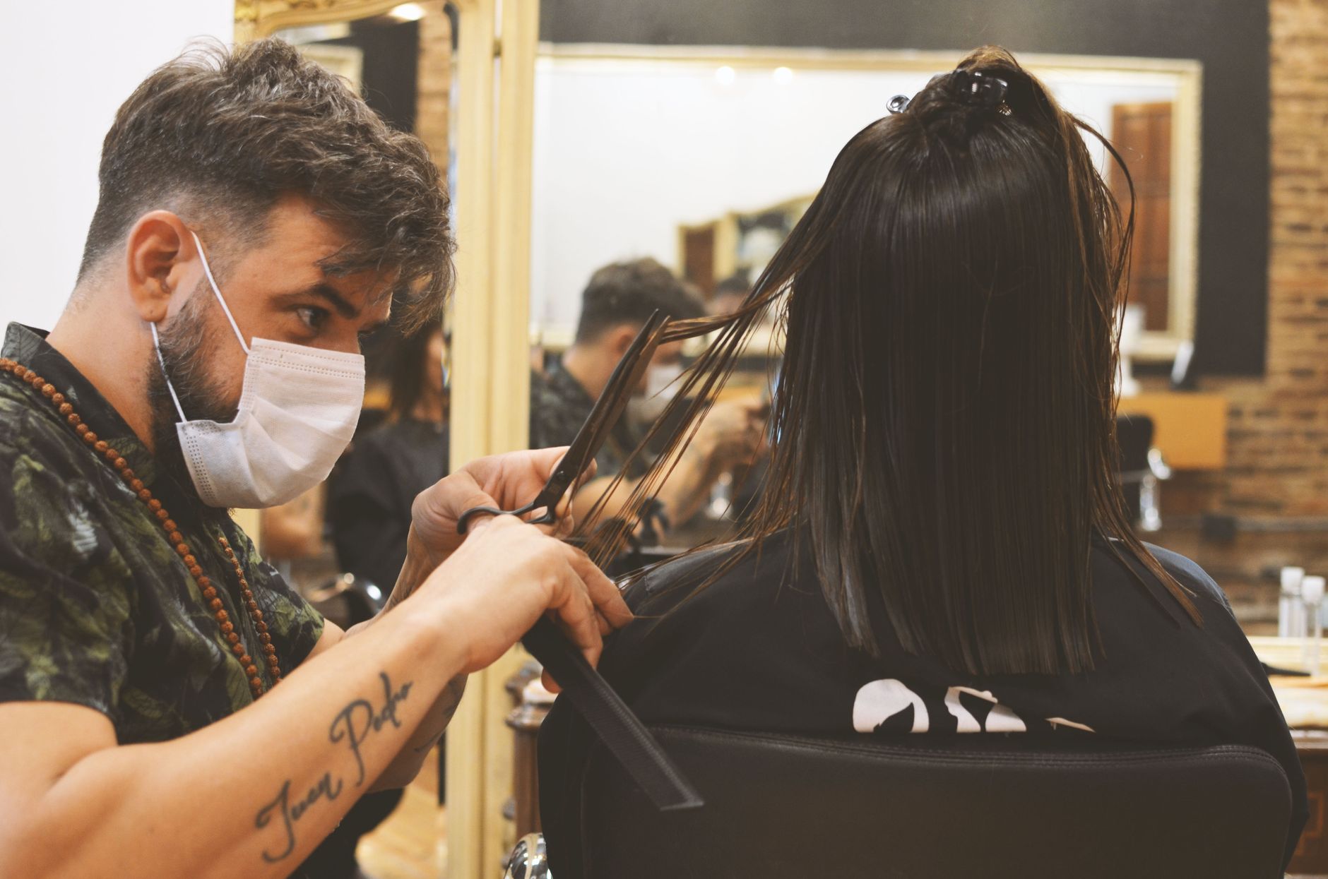 Health, safety and hygiene for aesthetic procedures — Barber wearing facemask carefully cuts woman's hair indoors, ensuring safety and style in a barbershop.