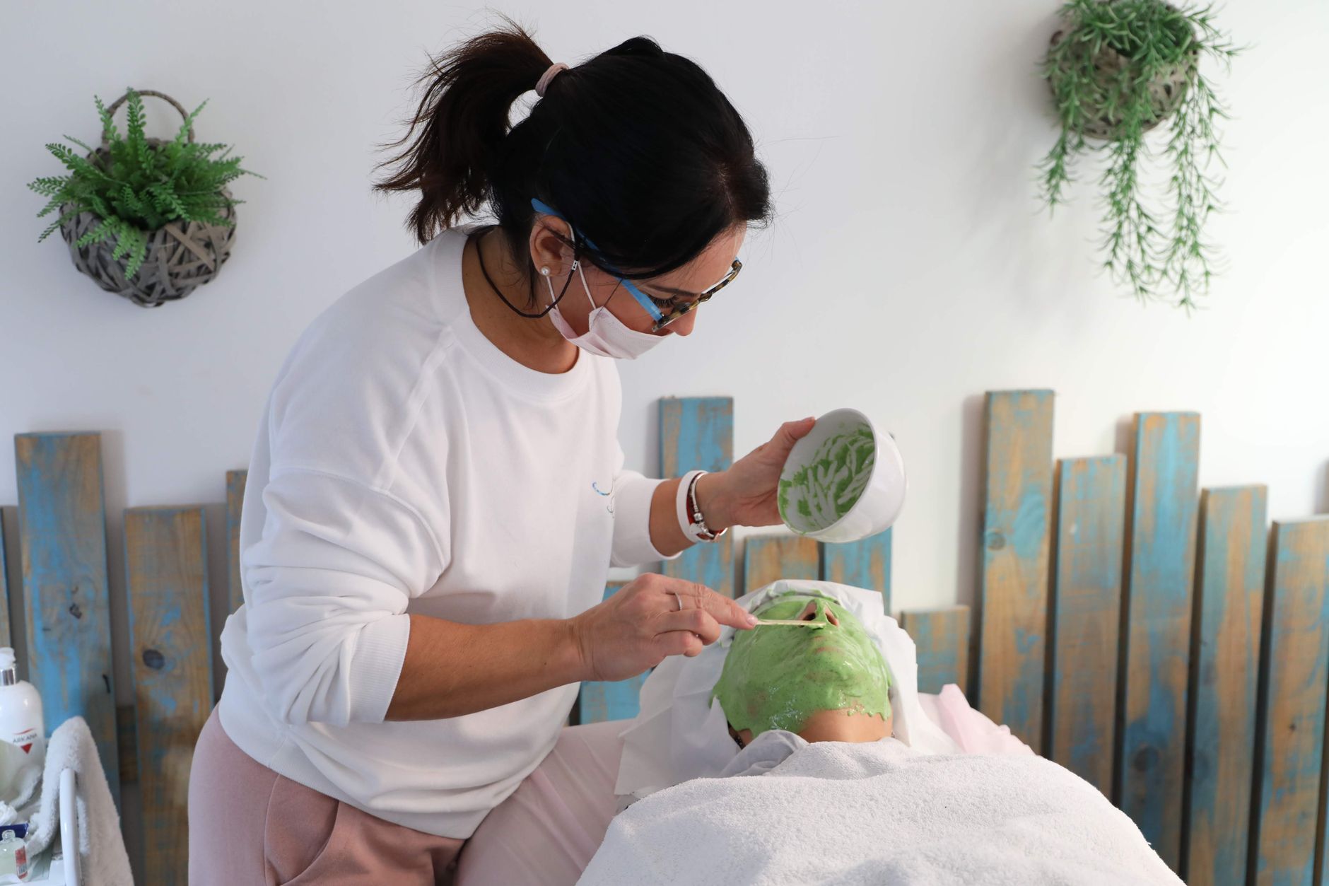 Professional, Ethical, and Sustainable Principles within Aesthetic Practice — Aesthetician applying a green clay mask to a client during a relaxing spa facial treatment.