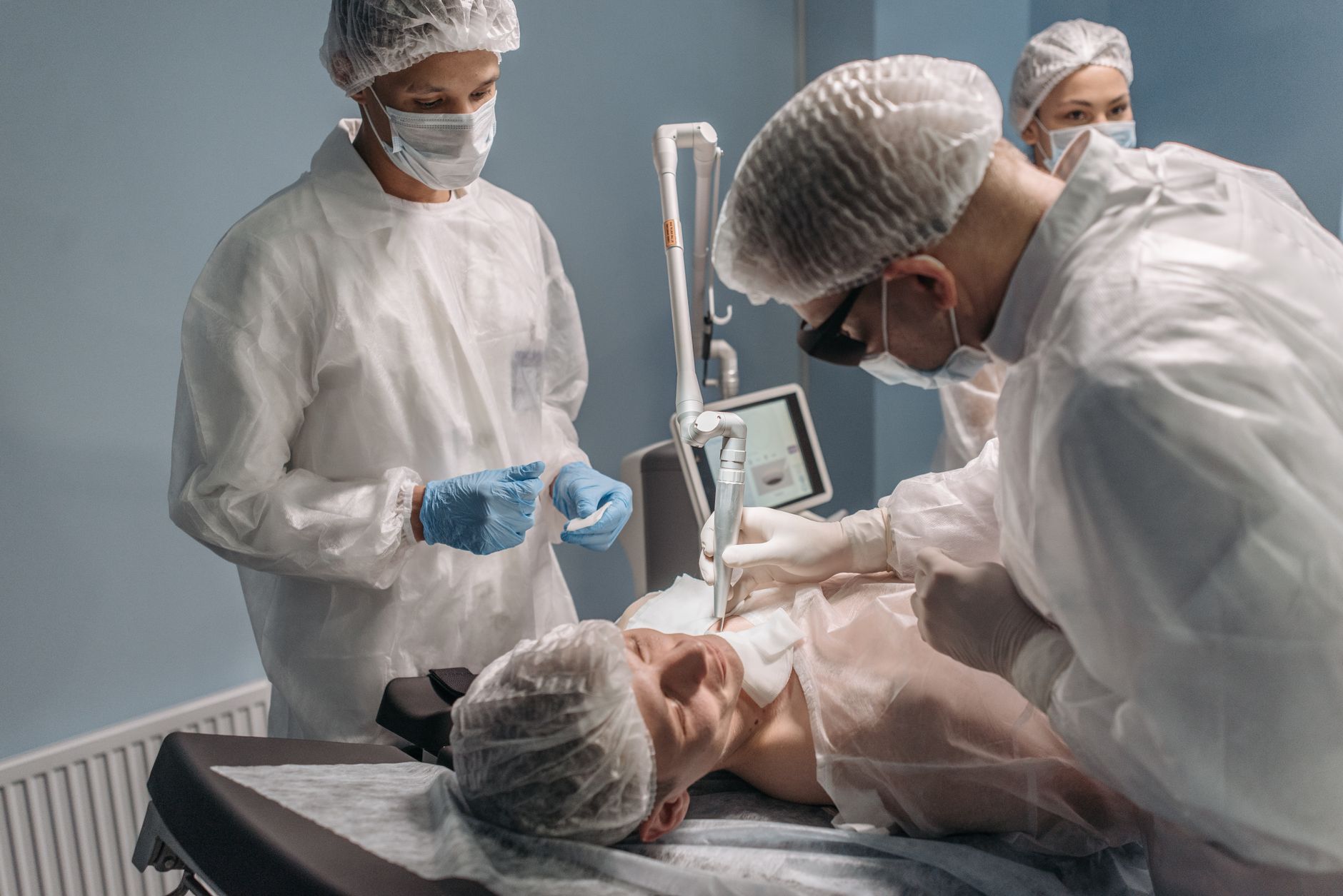 Advanced Aesthetic Procedures: Chemical Peels — A team of doctors performing a facial laser procedure in a sterile operating room.