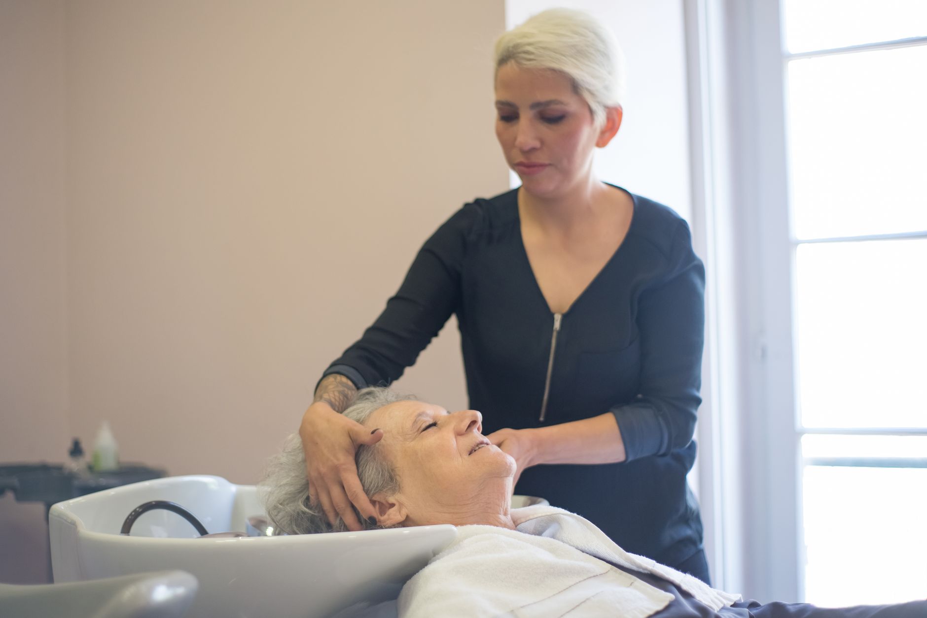 Anatomy and physiology — A hairdresser provides a relaxing washing service to an elderly woman in a salon.