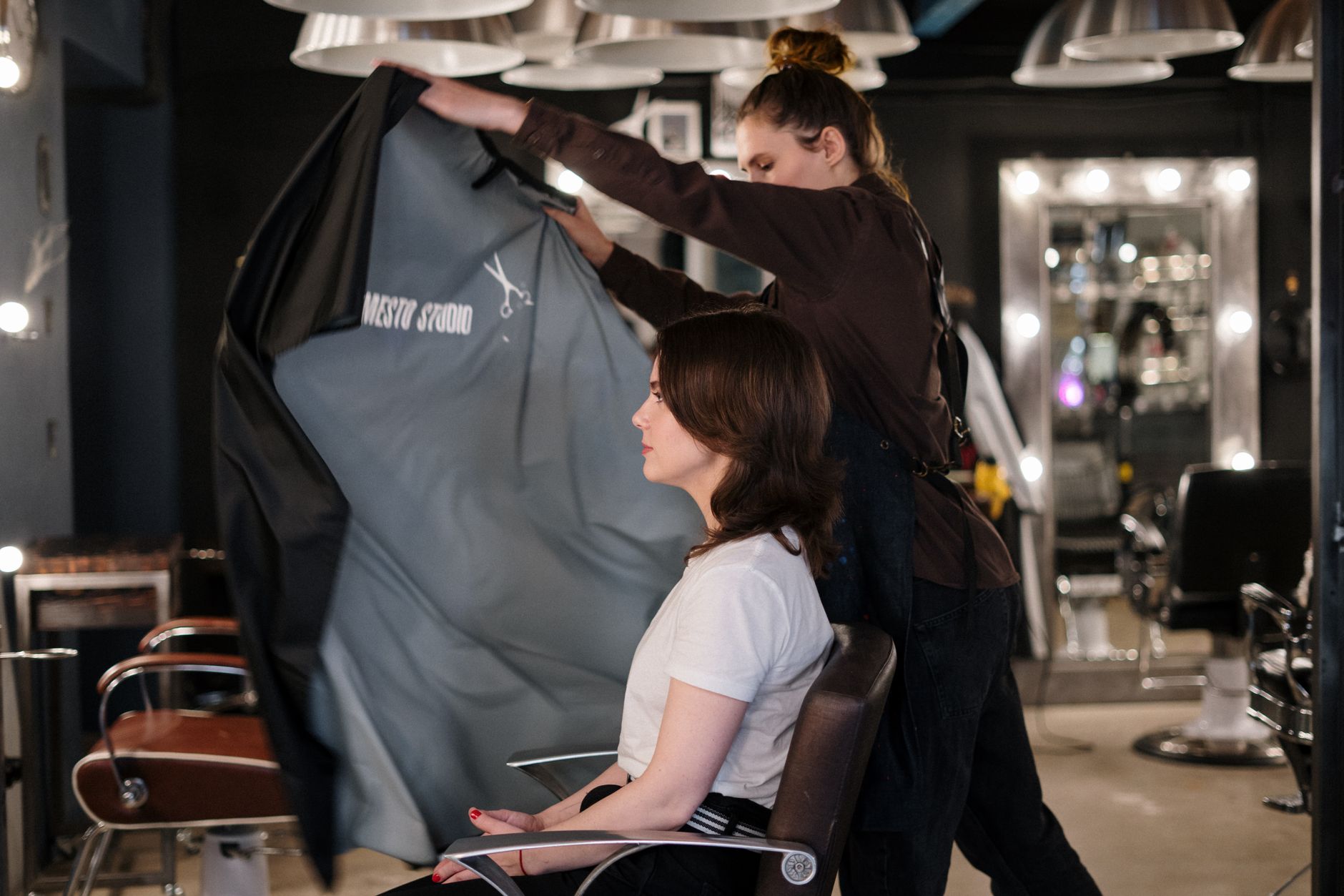 Health, safety and hygiene — Hair stylist draping cape over client for a haircut in a modern hair salon setting.