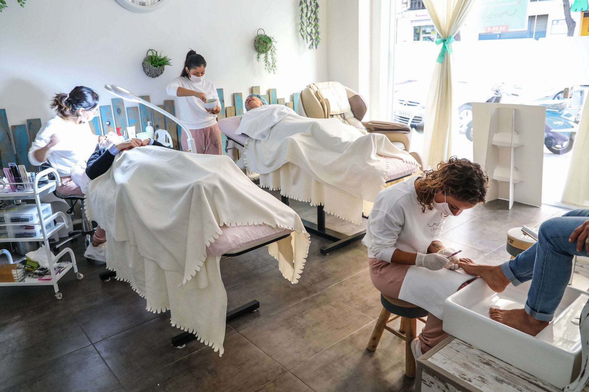 Waxing treatments — Peaceful spa scene with professionals giving facial and pedicure treatments in a well-lit salon.