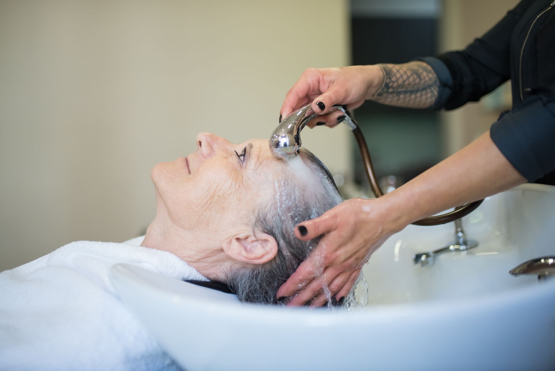 Lash and brow treatments — Elderly woman receiving a relaxing hair wash in a salon setting.