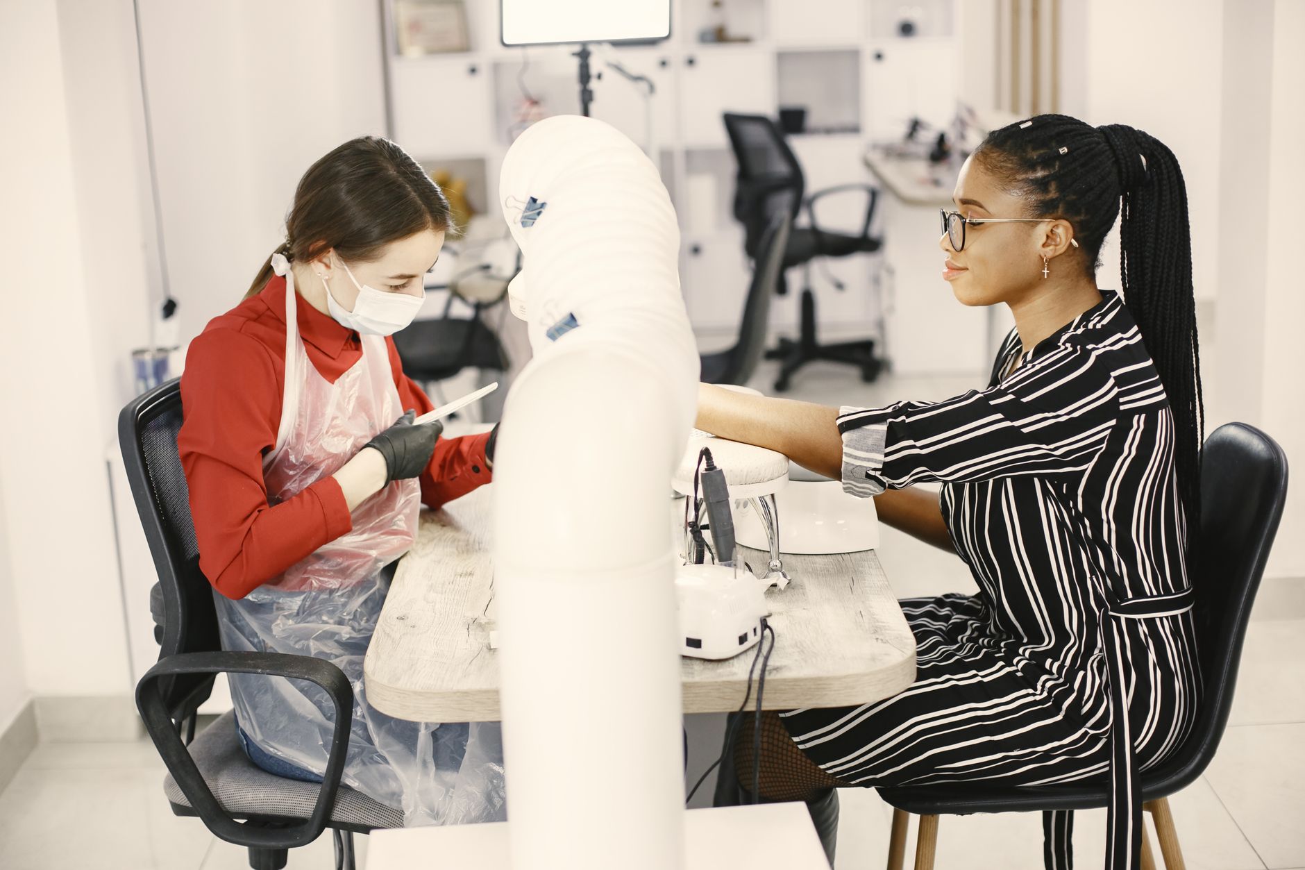 Freelance worker — A nail technician provides a manicure to a client in a stylish, modern nail salon.