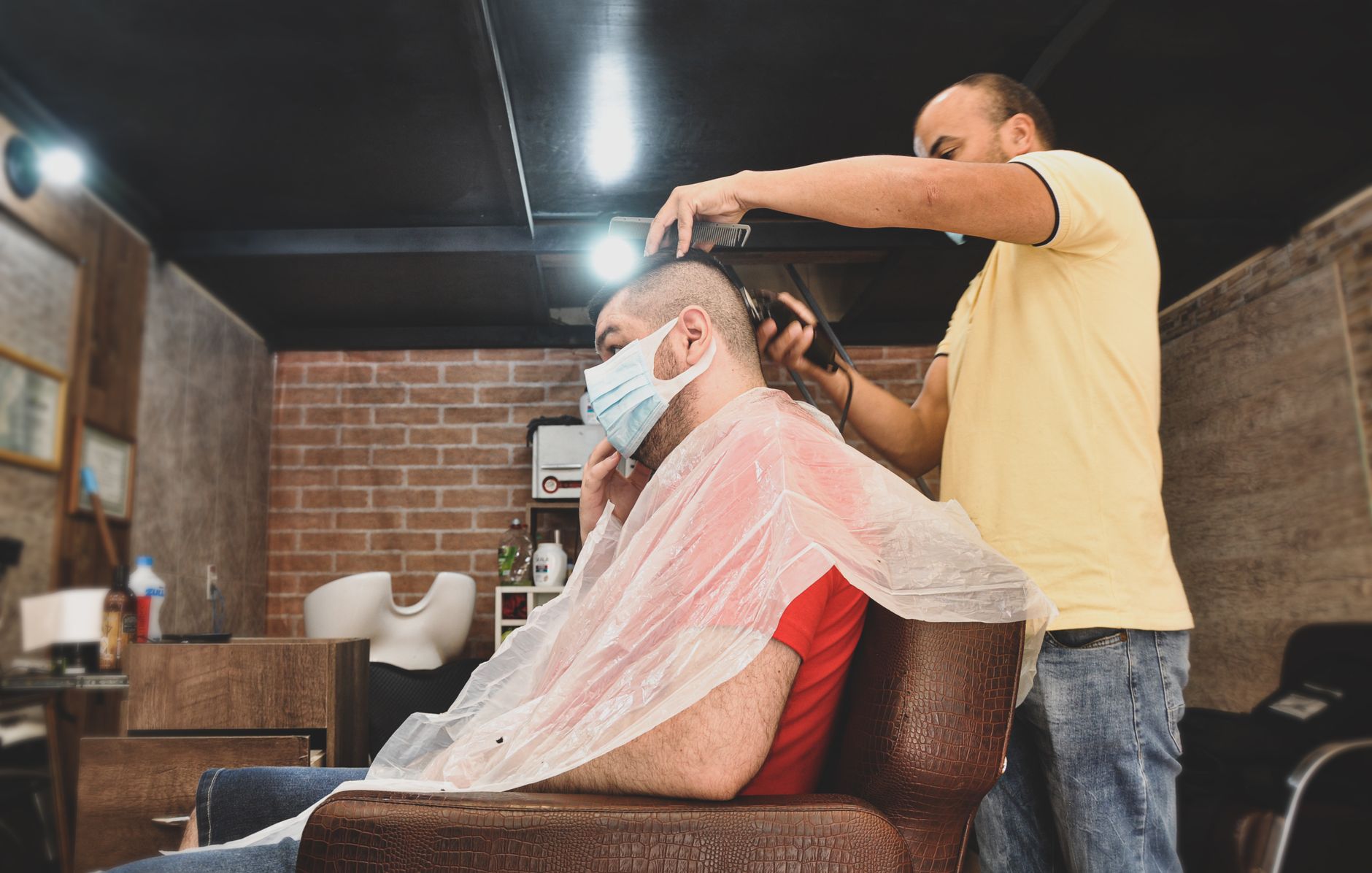 Health, safety, and hygiene — Barber trimming client's hair while both wear face masks in a cozy barbershop.