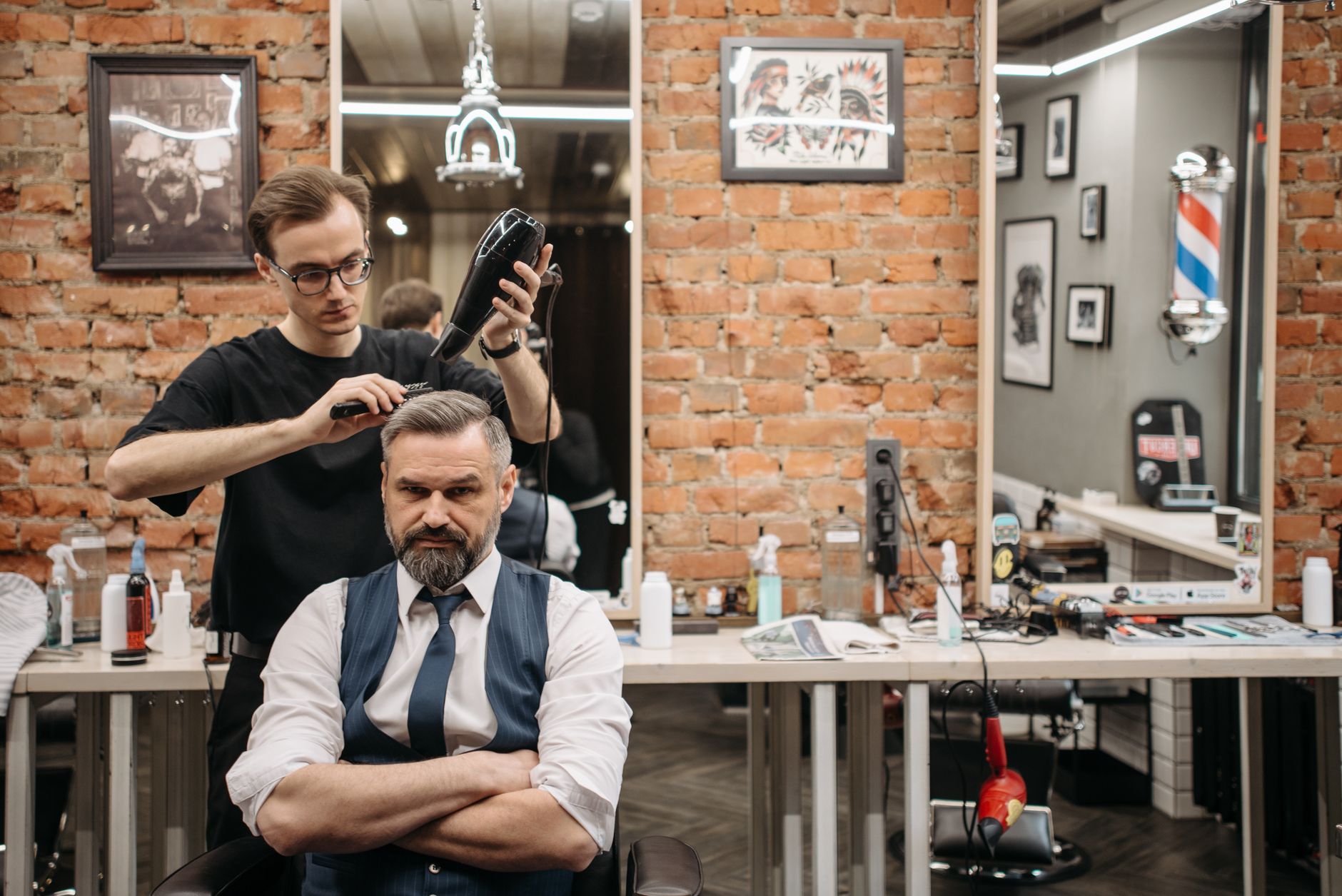 Blow-dry and finish hair — A barber professionally styling a man's hair in a modern barbershop setting.