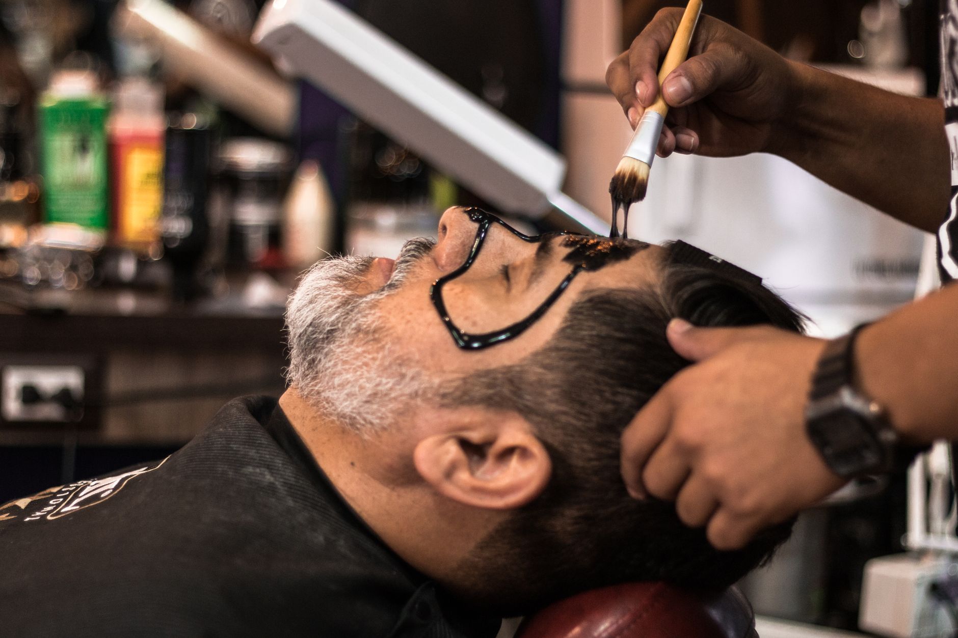 Health, safety and infection control for barbershops — A barber applies a facial mask to a man in a salon, promoting relaxation and skincare.