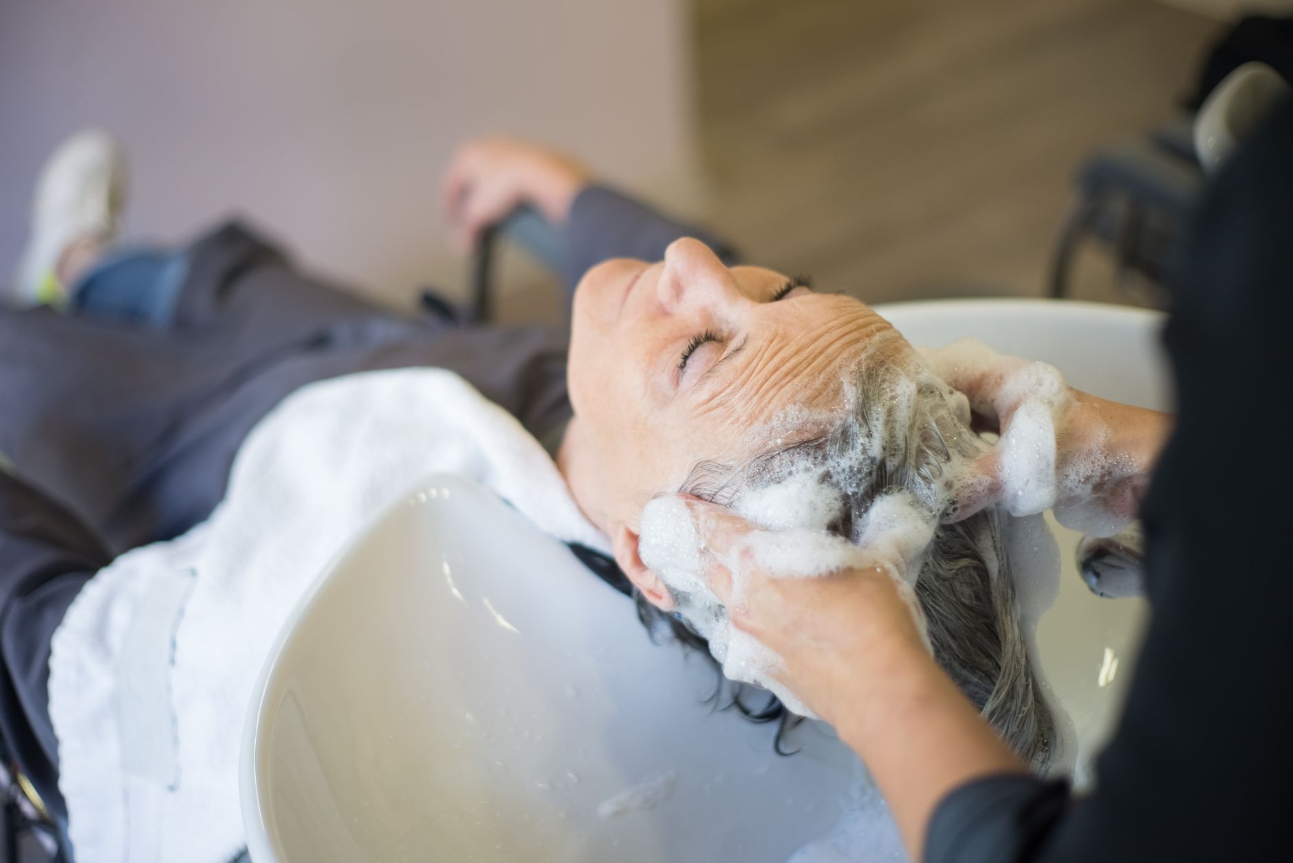 Shampoo, condition and treatment services for barbering — Woman enjoying a relaxing hair wash with shampoo and massage in a modern hair salon.