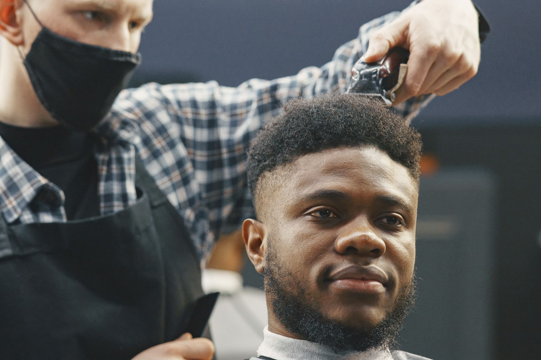 Introduction to barbering on a headblock — A barber trims a smiling man's hair using clippers in a professional setting.