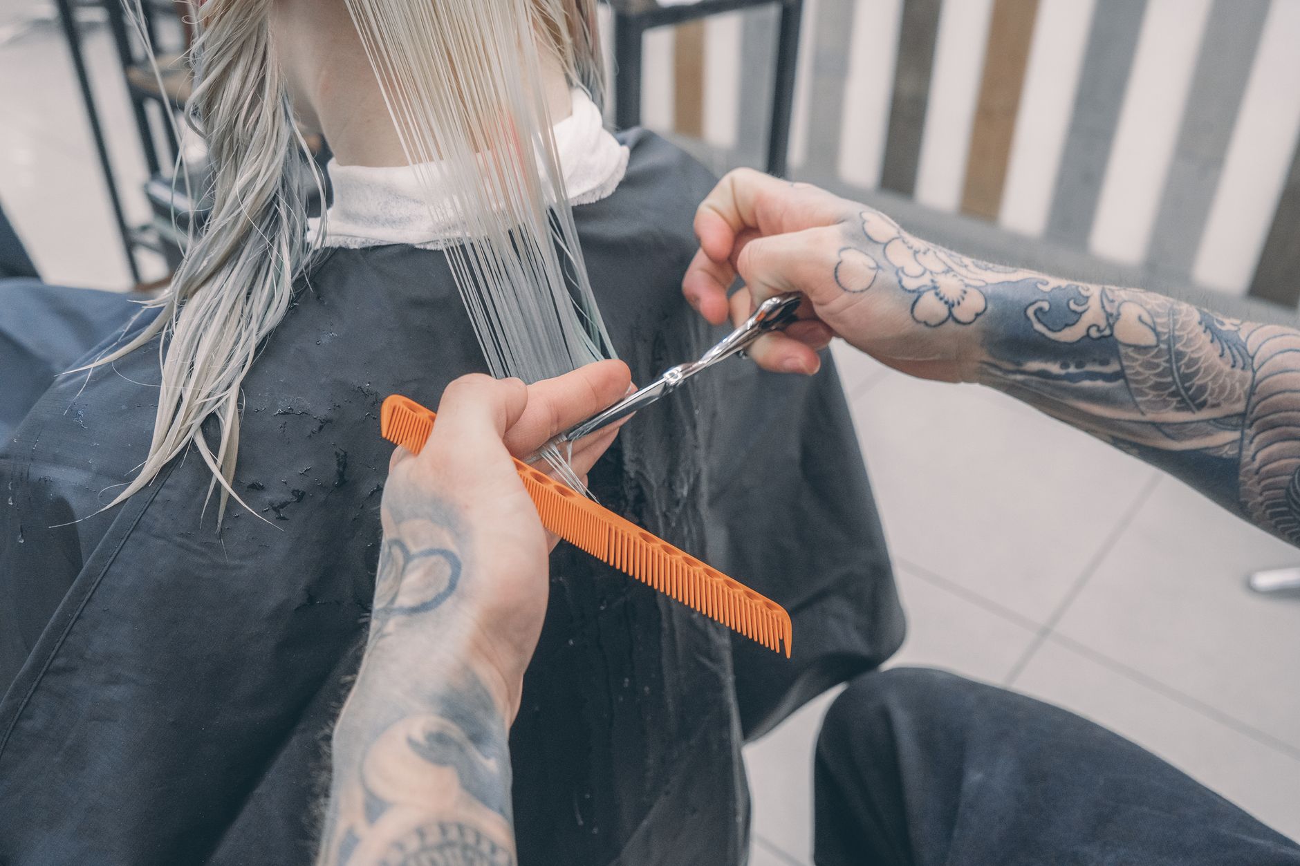 Modern barber haircuts — Close-up of a stylist's tattooed hands cutting wet hair in a modern beauty salon.