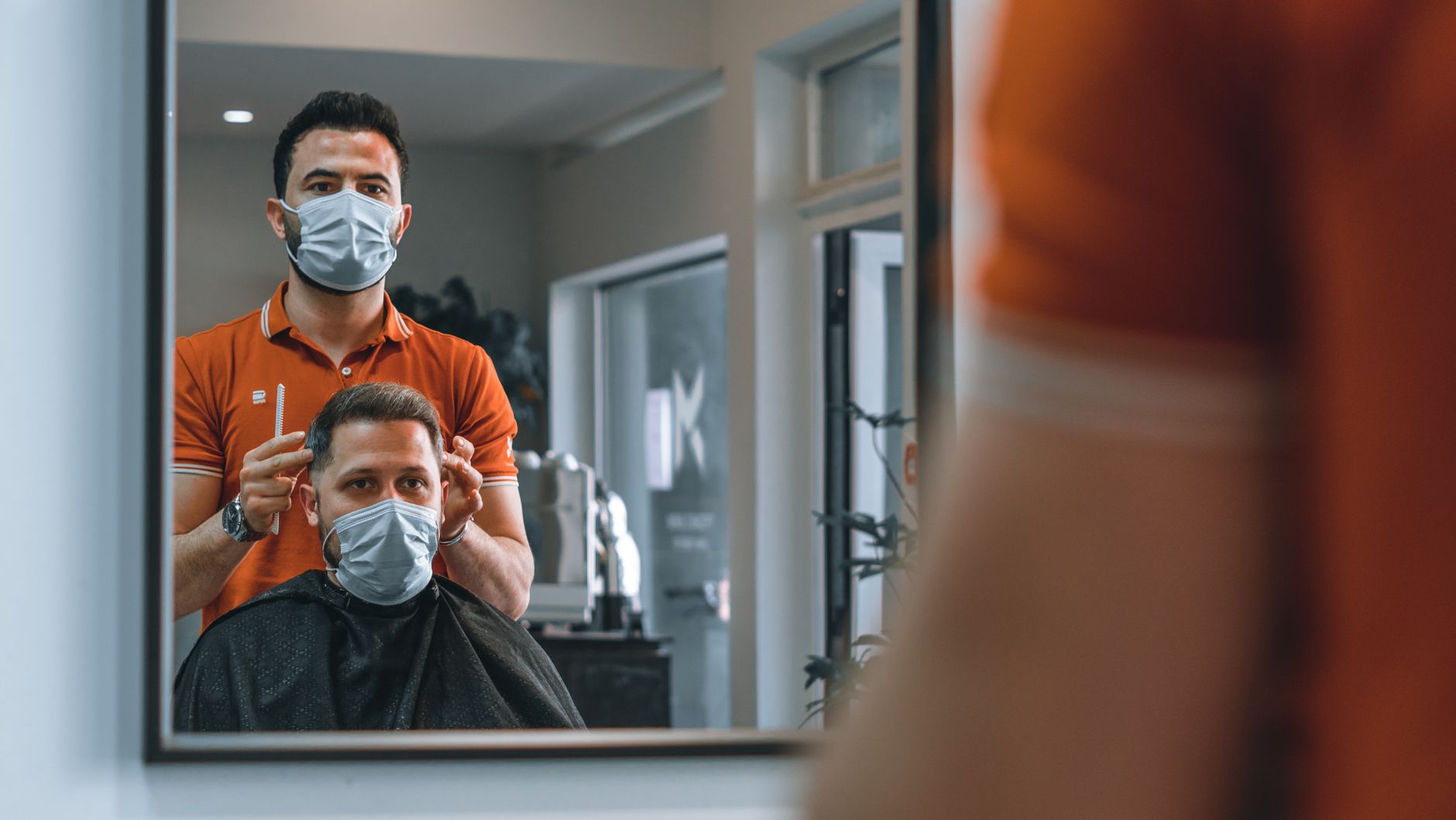 Implement health, safety, and hygiene — A barber wearing a mask cuts a client's hair in a modern salon, reflecting new hygiene norms.
