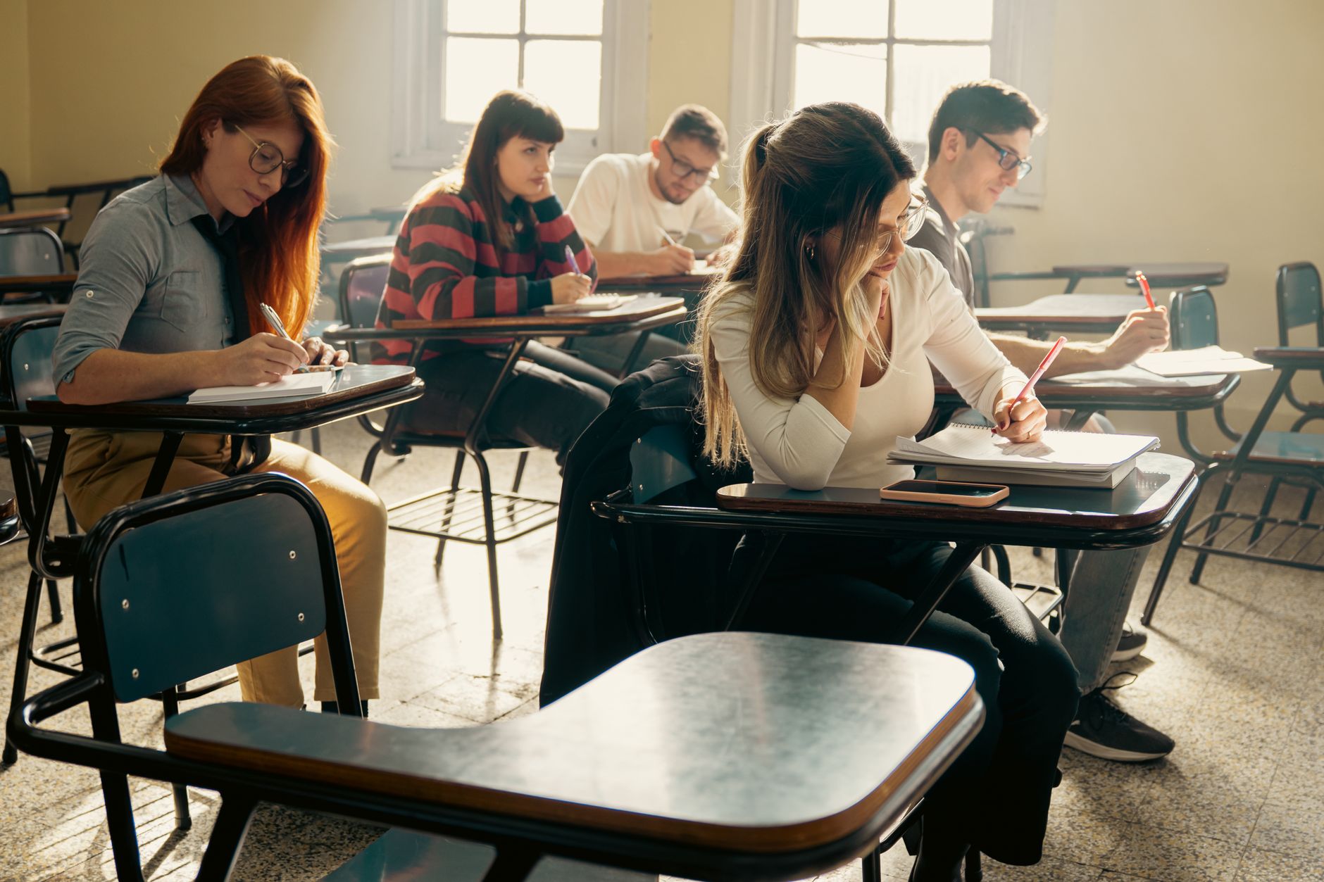 Client consultation and profiling — A diverse group of university students focuses on their studies in a sunlit classroom setting.