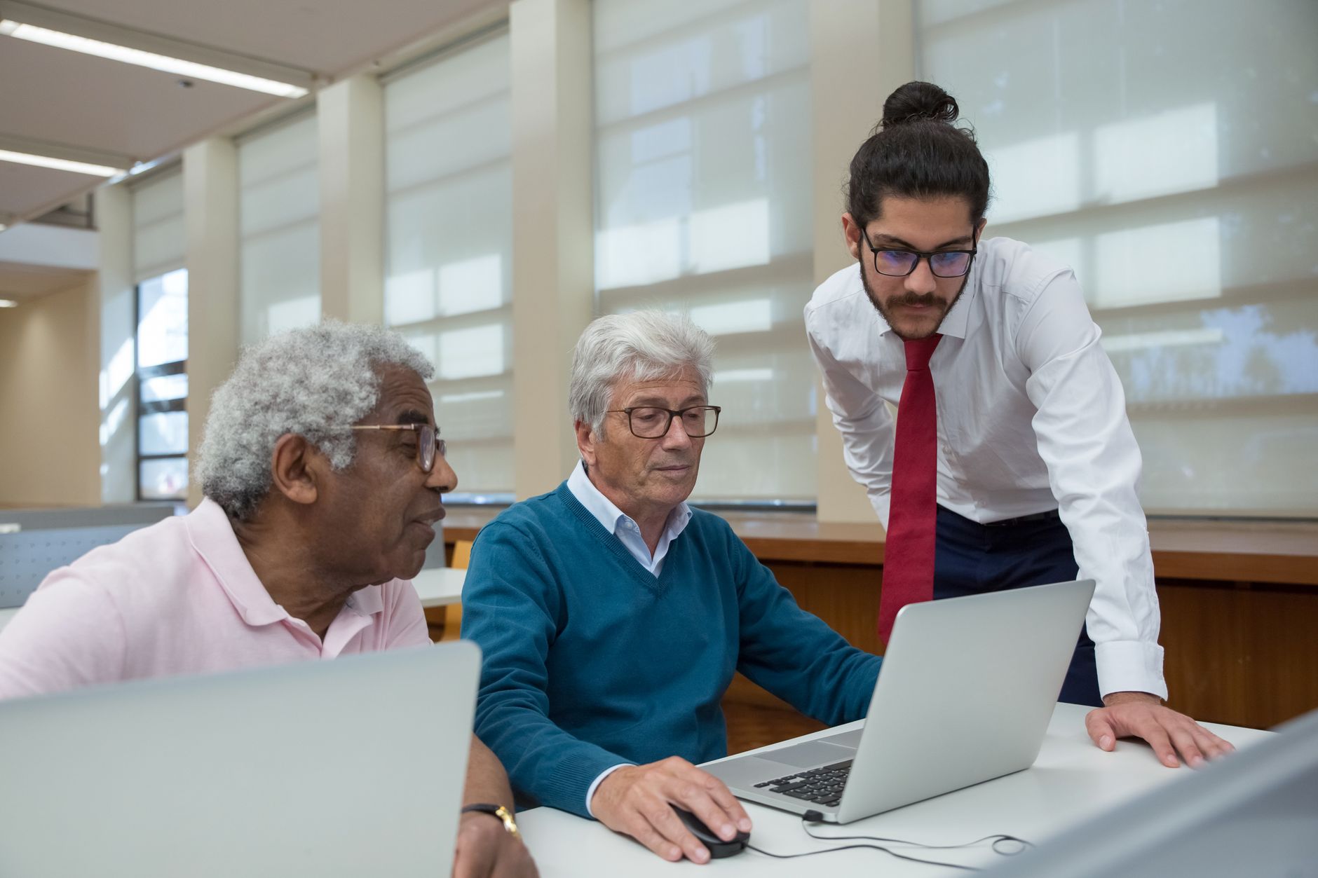 units and at least 3 — A diverse group of seniors learning with a tutor in a library, using laptops to study.