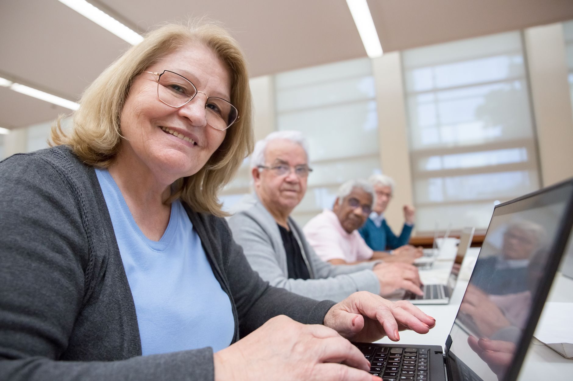 Psychology and Wellbeing Foundations — Group of senior adults using laptops for a digital learning session in a modern indoor setting.