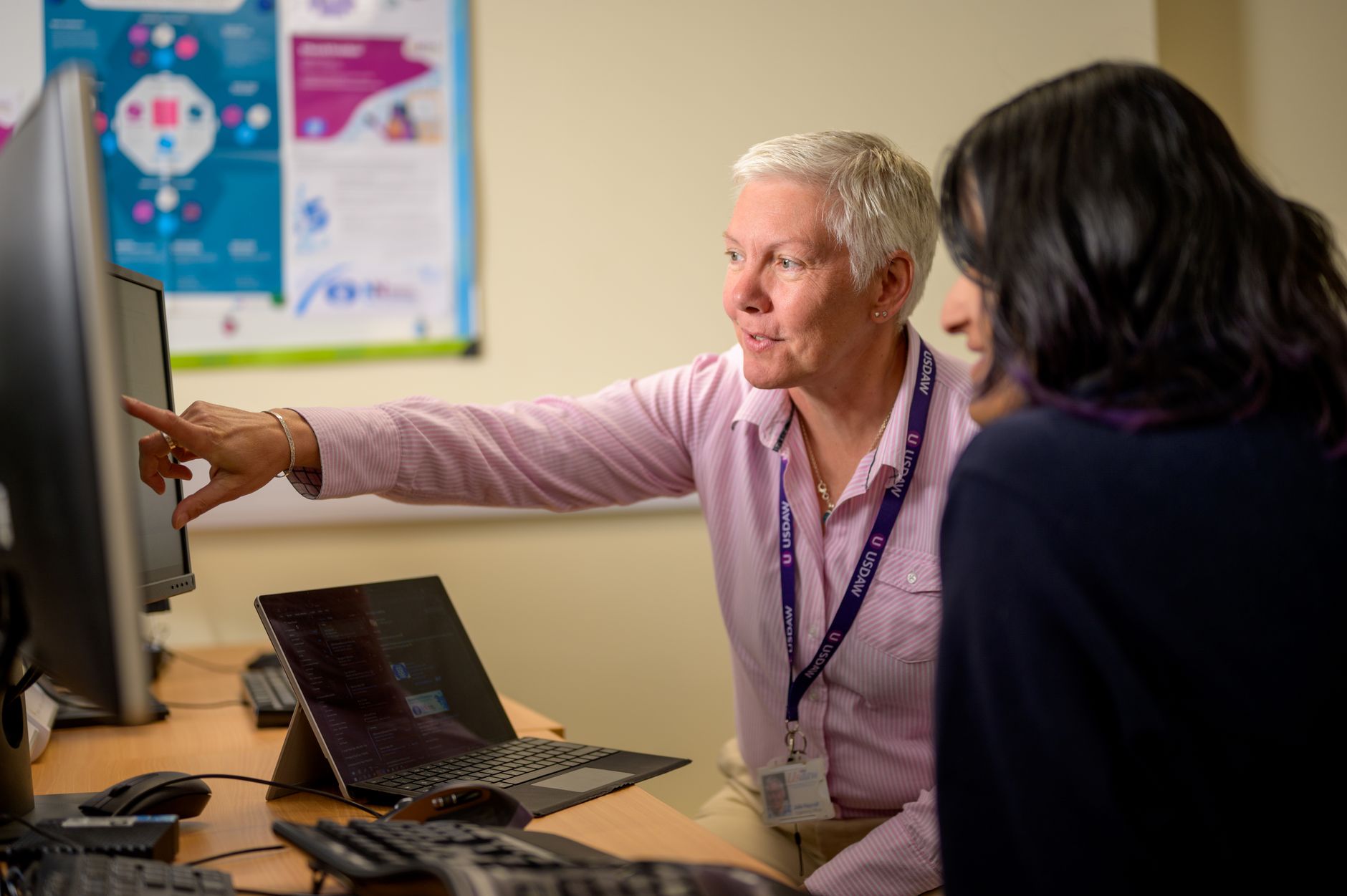 Coach Training for Professional Accreditation — Two women collaborating at a desk in a modern office setting, using technology.
