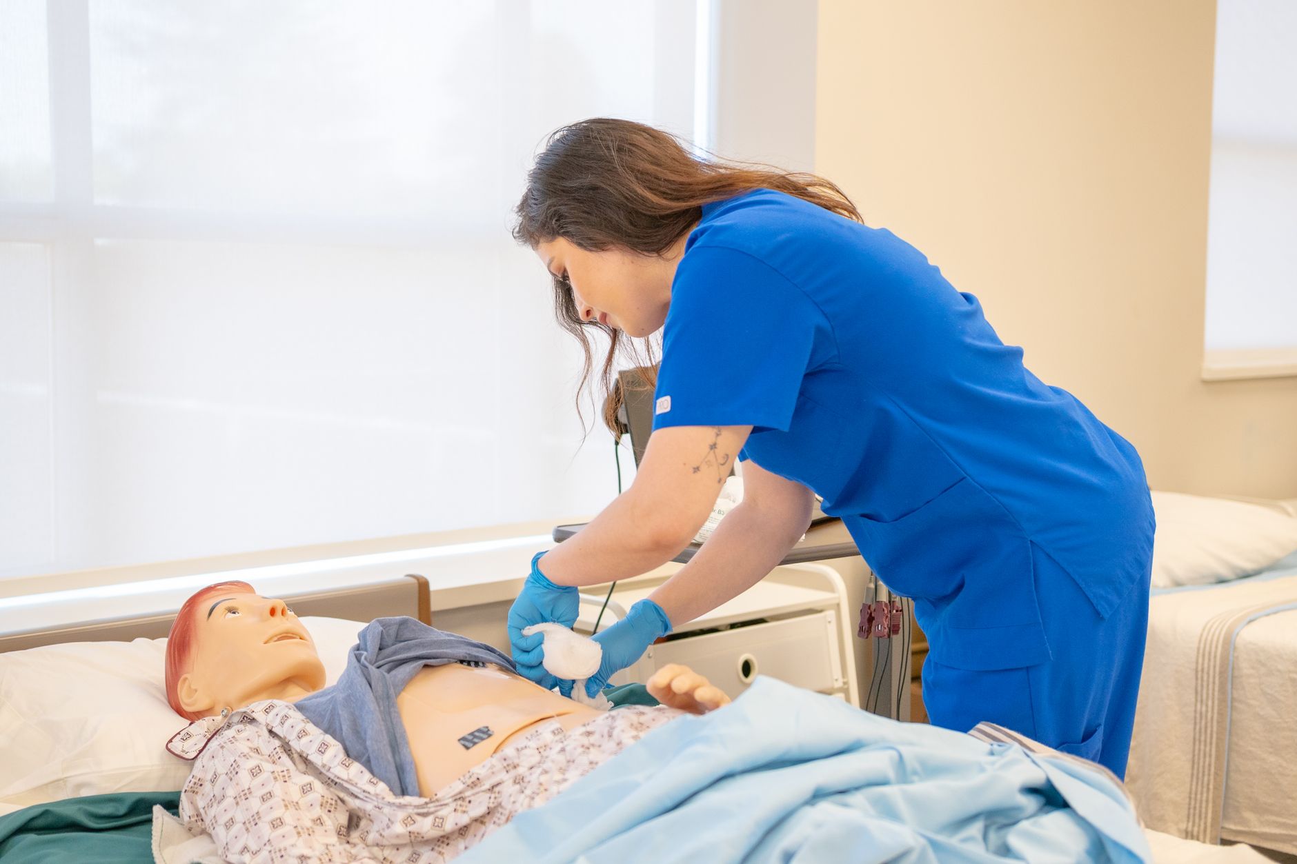 Adult Education — A nurse in blue scrubs practicing medical procedures on a hospital training manikin.