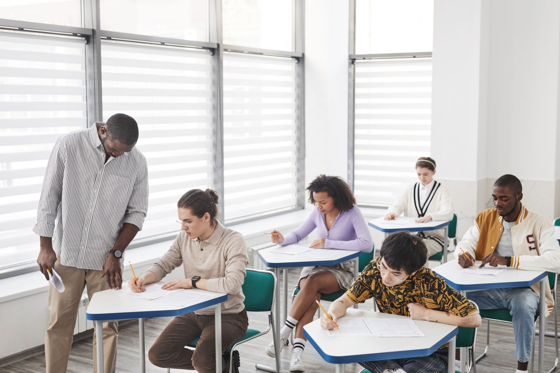 Understanding the Principles and Practices of Externally Assuring the Quality of Assessment — A diverse group of students taking a test in a classroom with a teacher assisting.