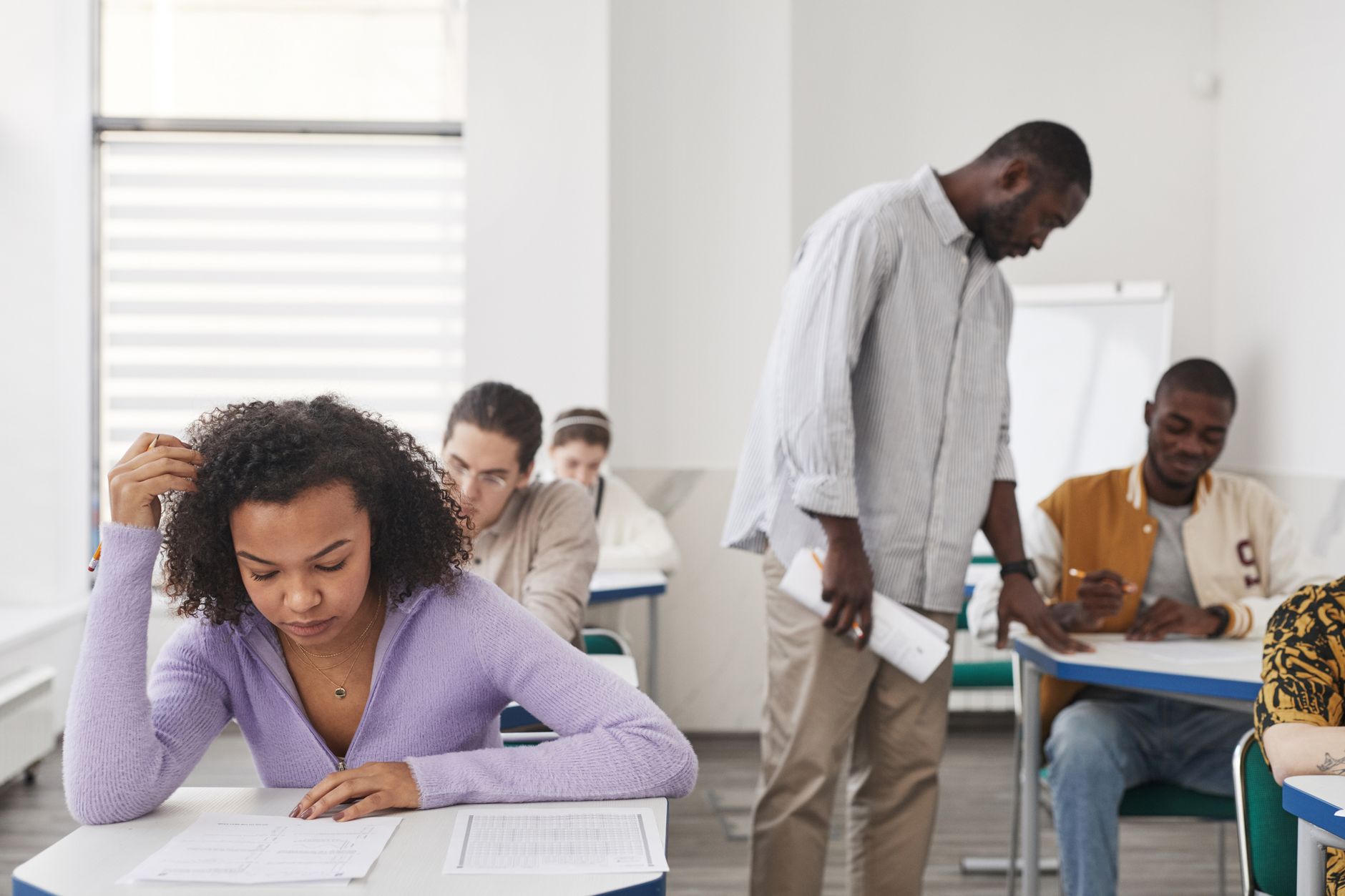 Externally Assure the Quality of Assessment — A diverse group of students taking an exam in a modern classroom with a teacher supervising.